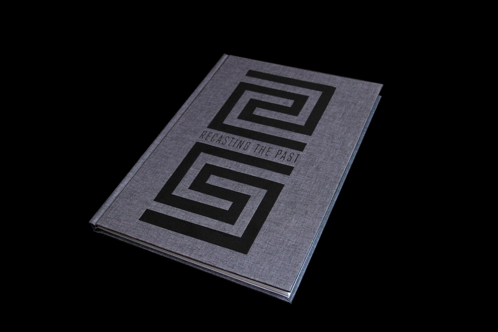 Gray hardcover book titled "Recasting the Past" with black geometric patterns on the cover, placed against a black background.