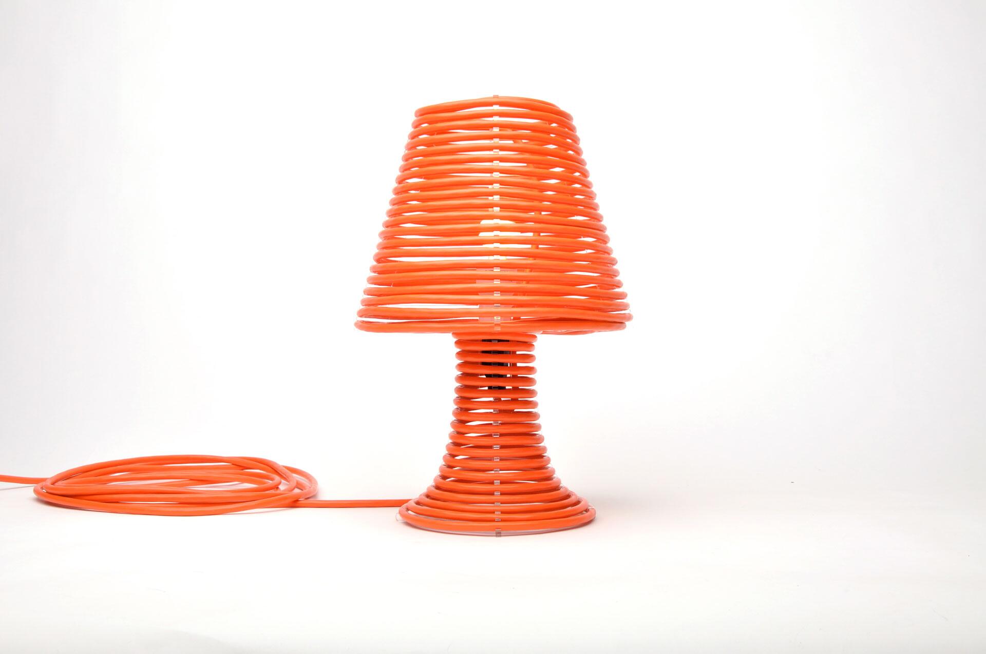 Orange desk lamp made from coiled wire, shaped into a cone with a circular base, against a white background.
