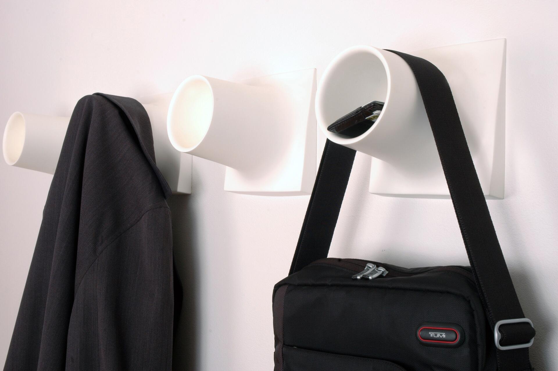 Wall-mounted coat hooks with tubular design holding a dark jacket, a smartphone, and a black bag with a strap.