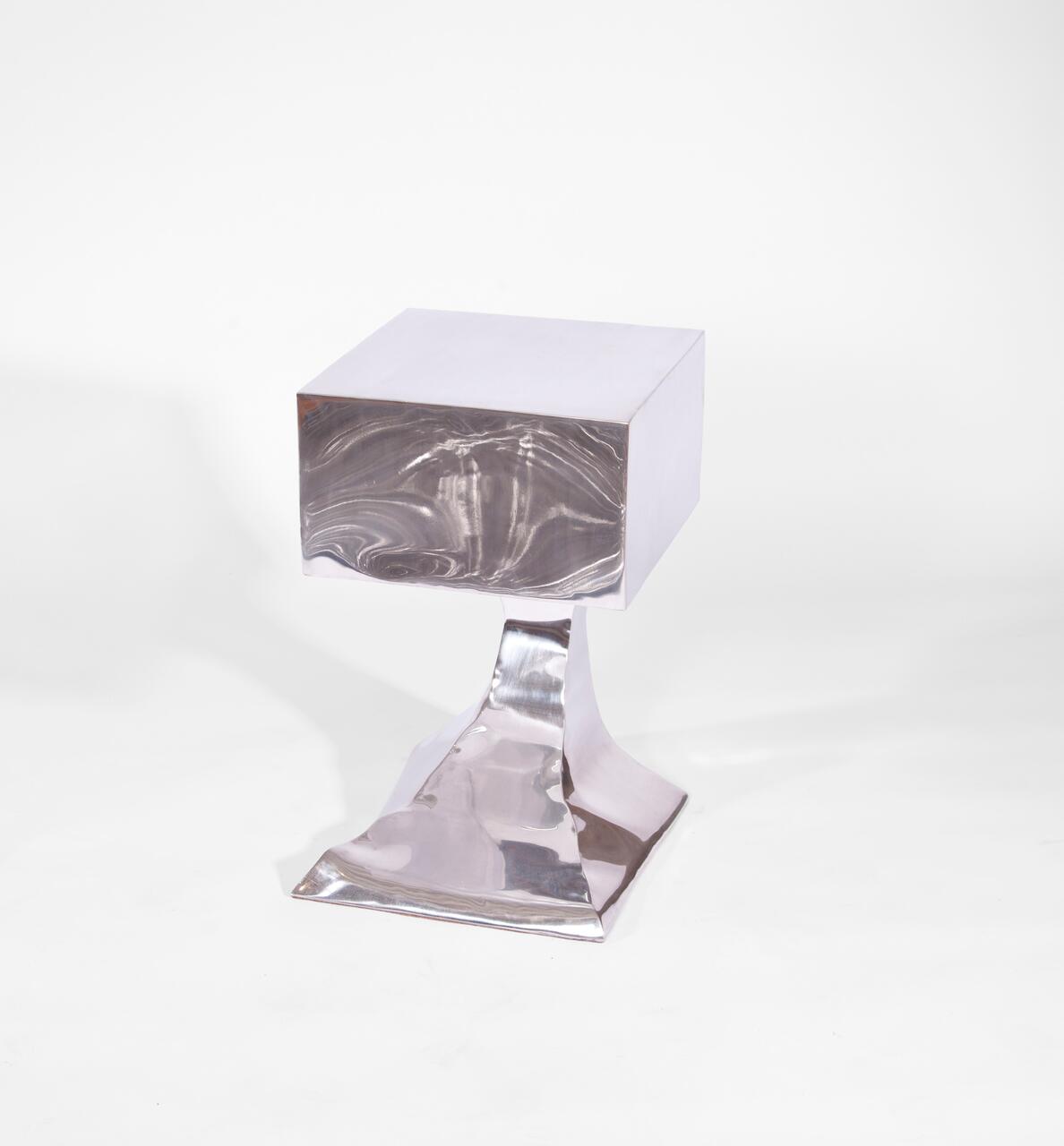 Shiny metallic sculpture with a cube top on an abstract curved base, set against a plain white background.