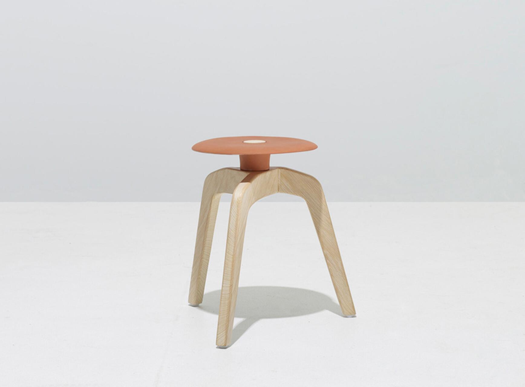 Modern wooden stool with three legs and a round, terracotta-colored seat on a light gray background.