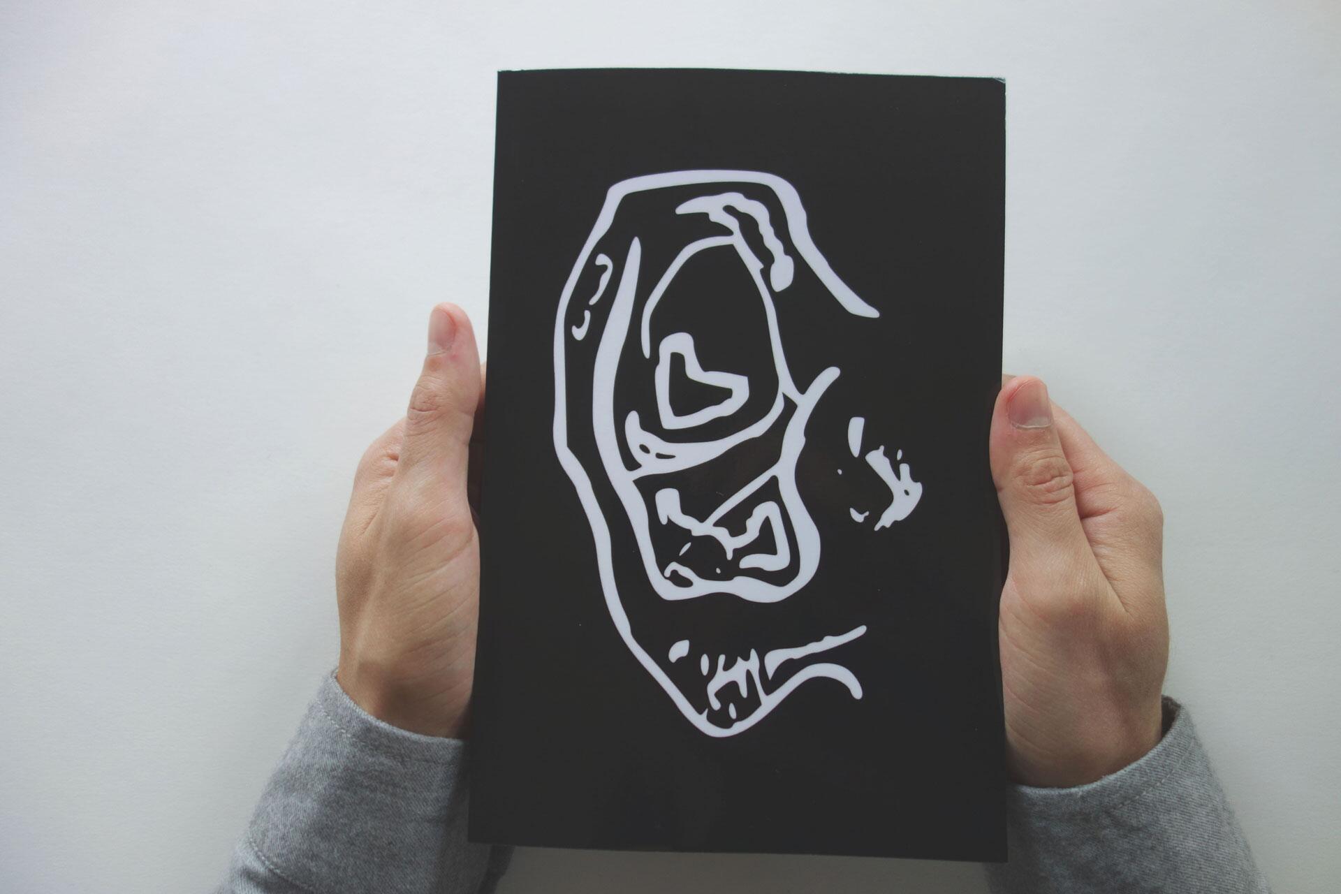 Hands holding a black book with abstract white line art on the cover against a white background.