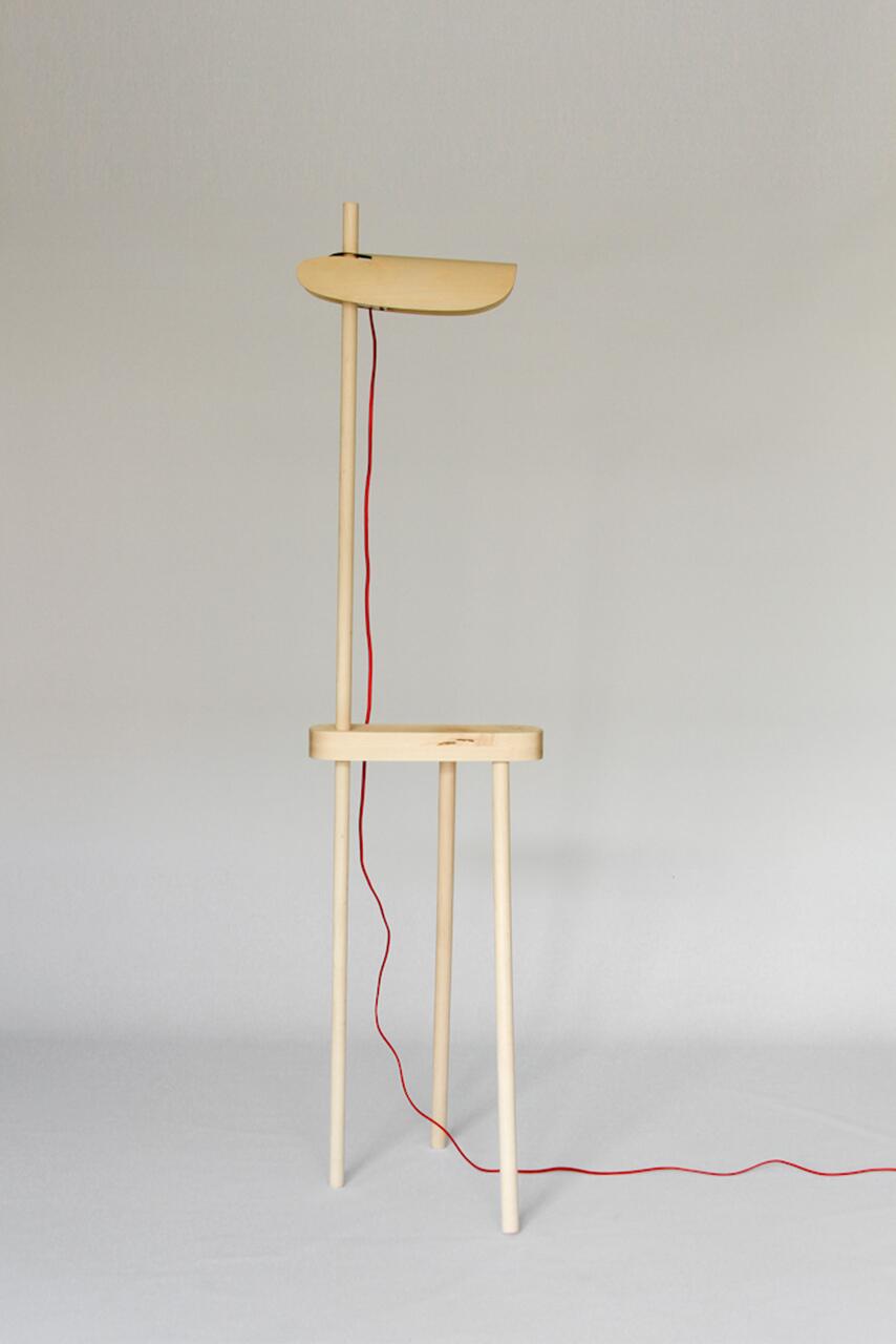 Minimalist wooden coat rack with three legs, featuring a small shelf and a red cord hanging from the top, set against a plain background.
