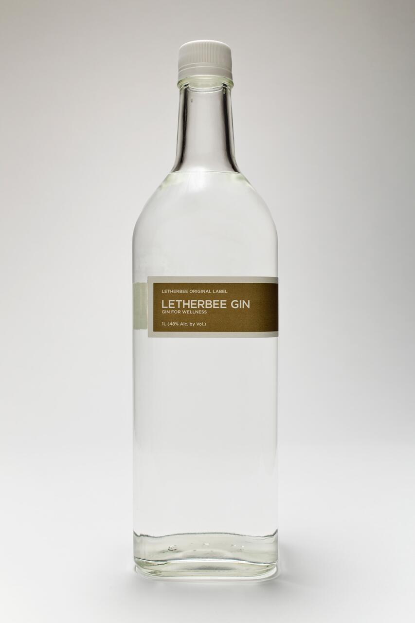 Clear glass bottle of Letherbee Gin with a simple brown label, white cap, and transparent liquid inside, set against a neutral background.