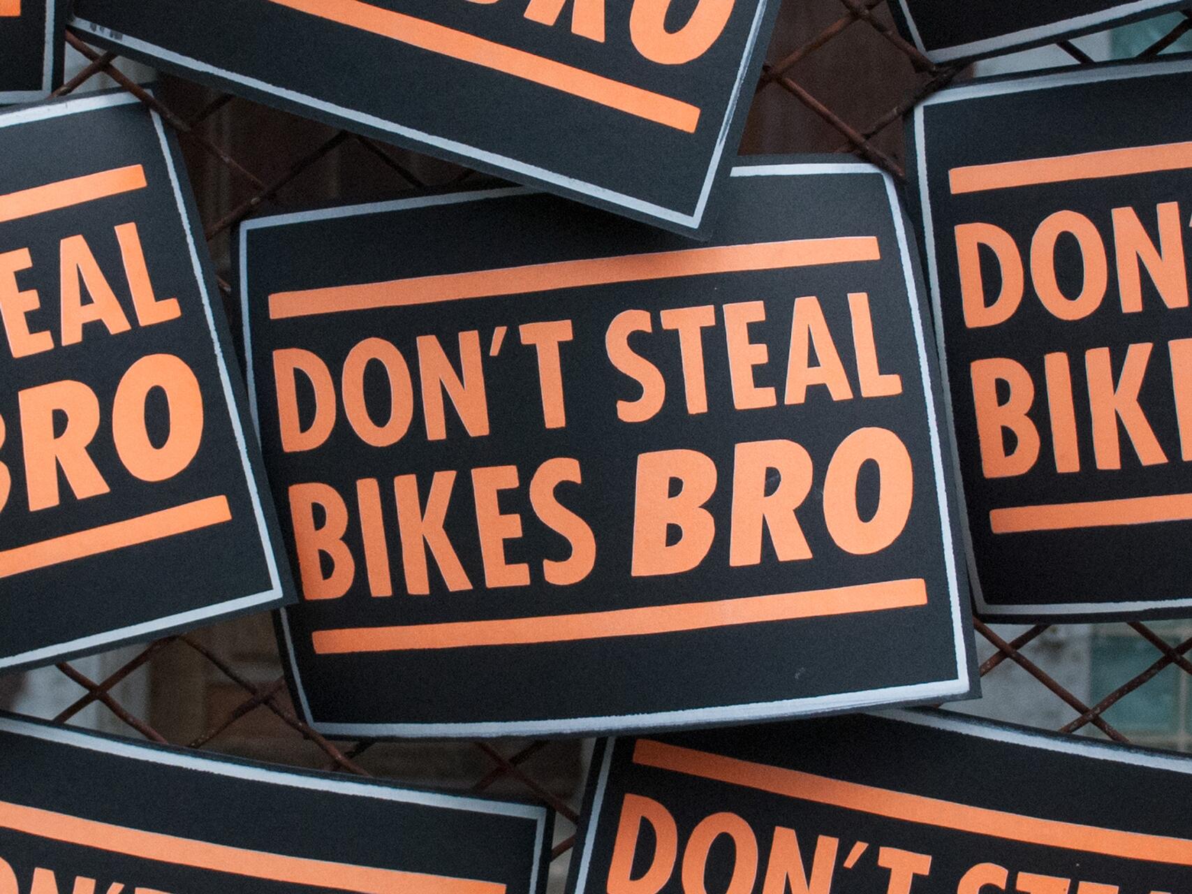Signs with bold orange text on black background, reading "DON'T STEAL BIKES BRO," layered over each other.
