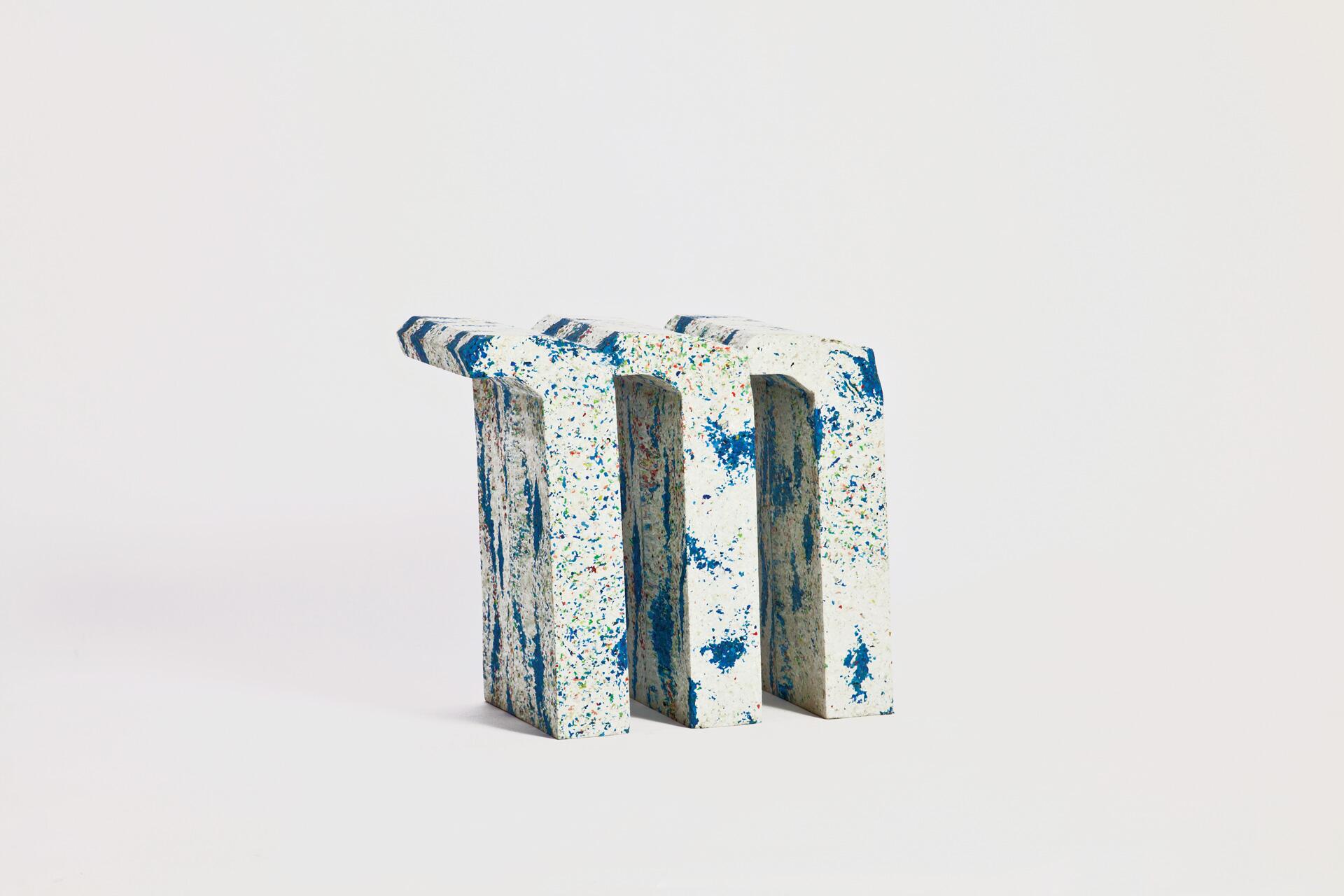 White and blue textured sculpture with a speckled pattern, consisting of three vertically standing rectangular blocks with arch-shaped cutouts, set against a plain background.
