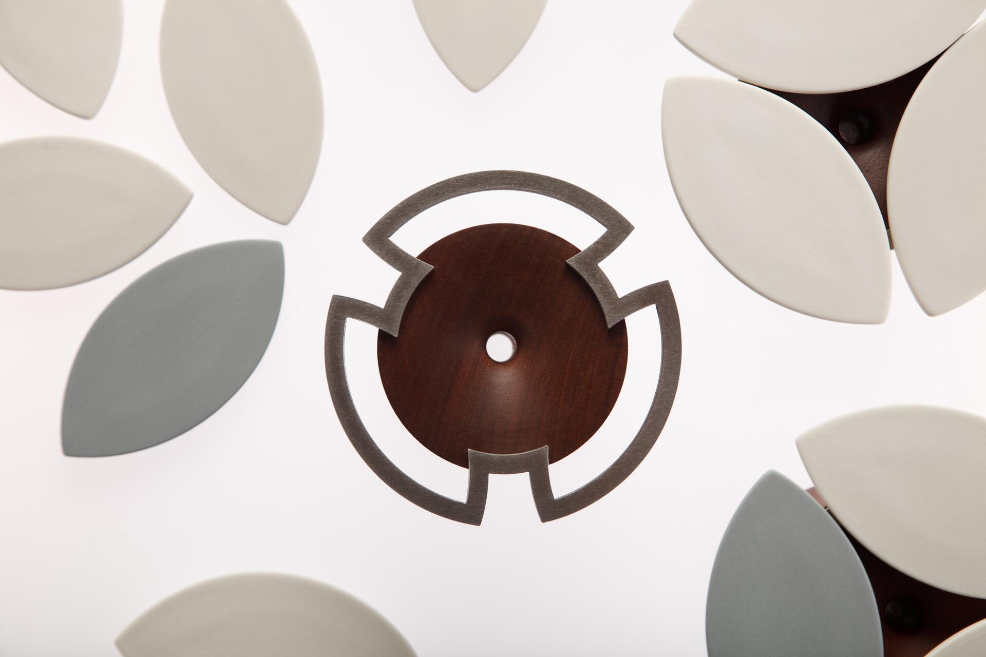 Abstract geometric design with leaf-shaped elements in beige and gray surrounding a central brown circle with a decorative cutout, all on a white background.
