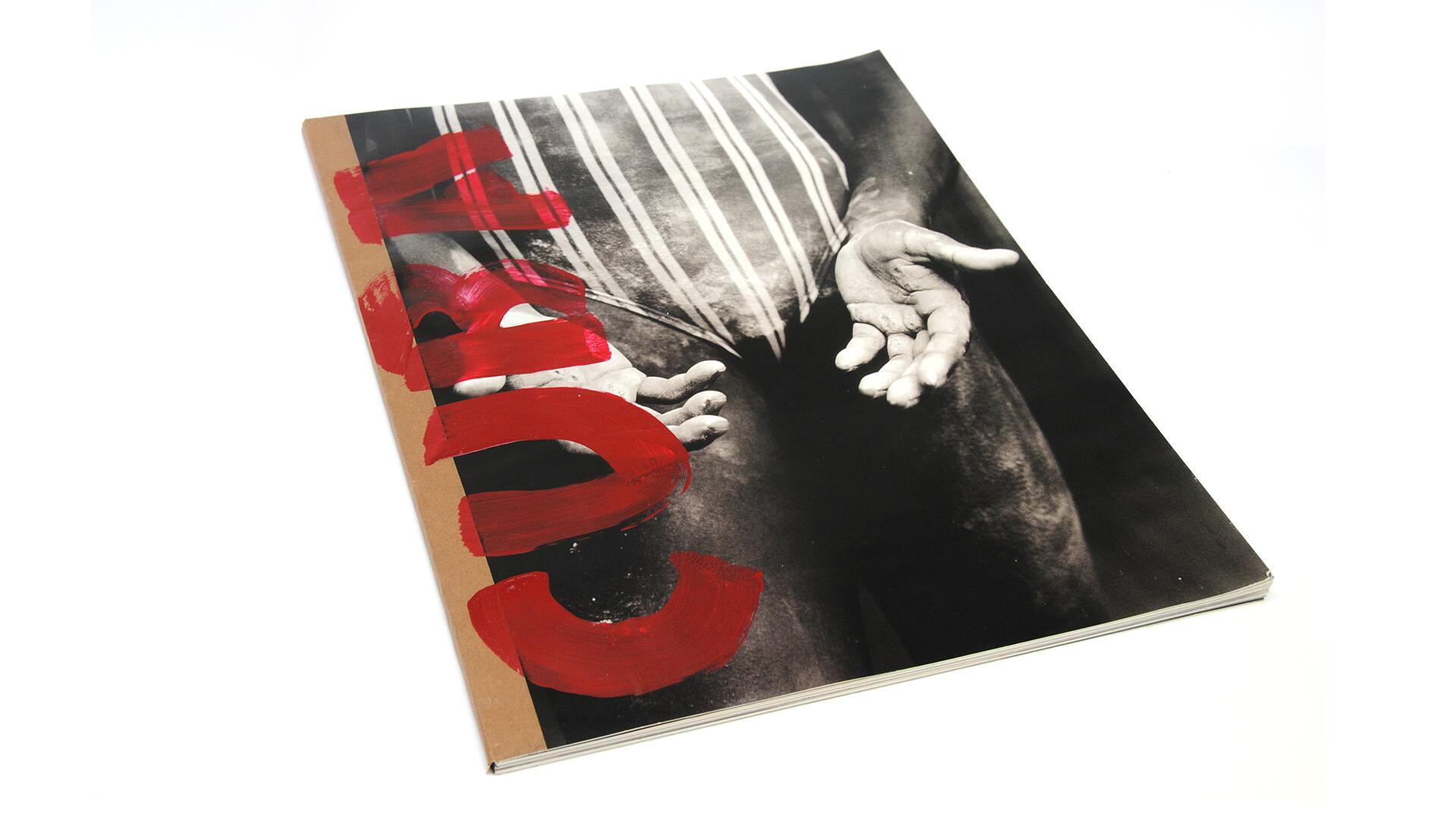 Black and white photograph of open hands against a striped garment, overlaid with bold red paint strokes.