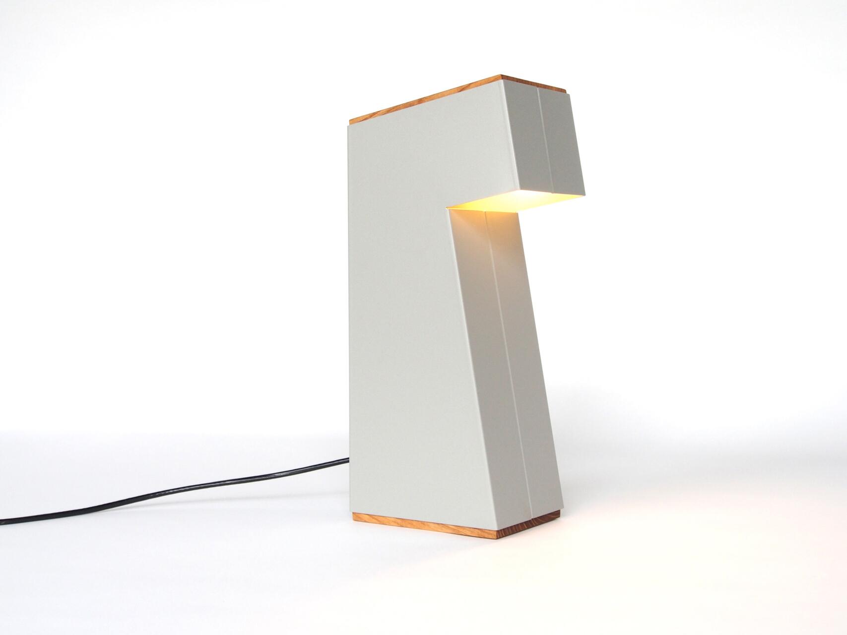 Minimalist gray table lamp with a geometric design, featuring a wooden base and top, softly illuminating from a concealed light source on a white background.