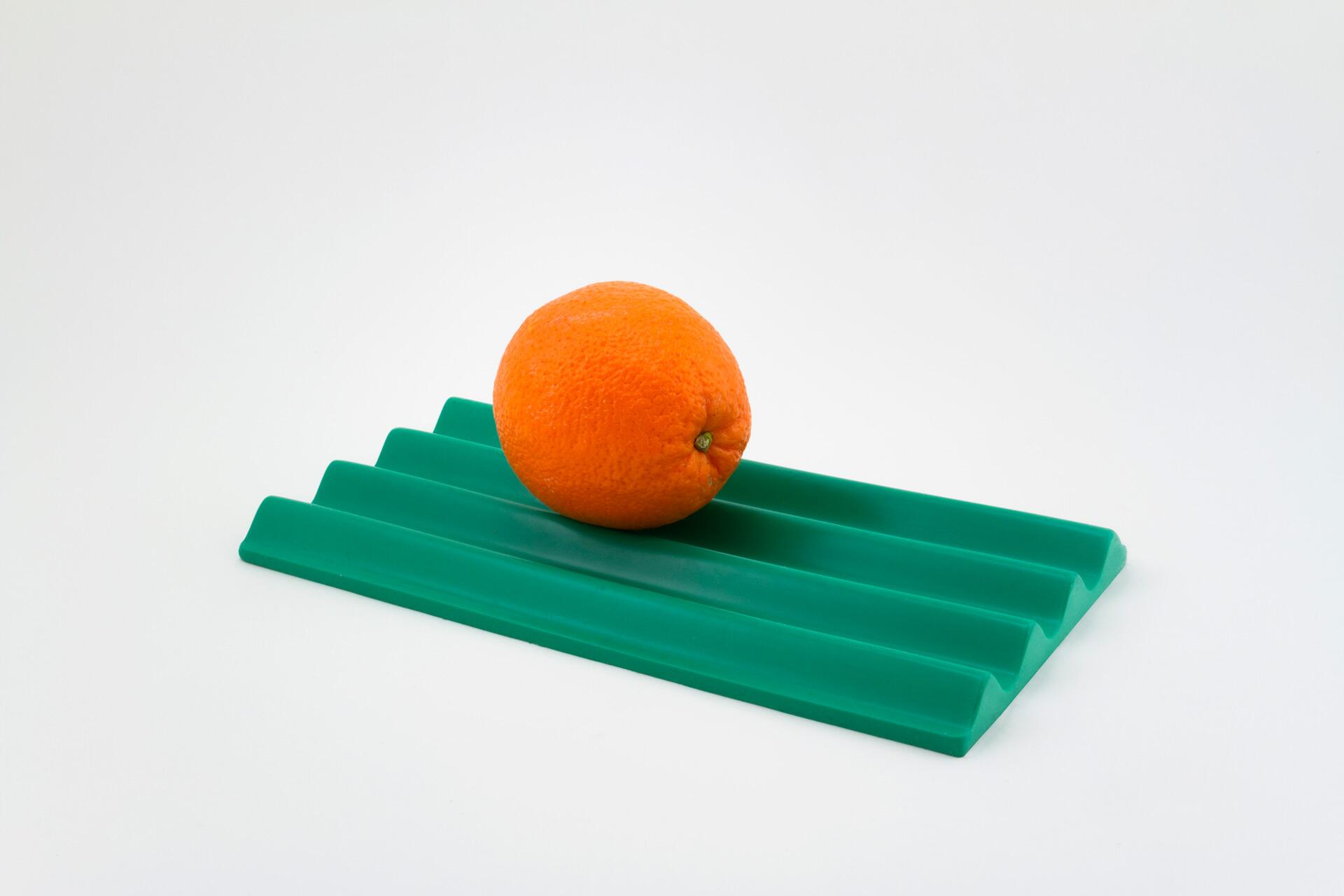 Orange fruit on a green, ridged silicone mat against a white background.