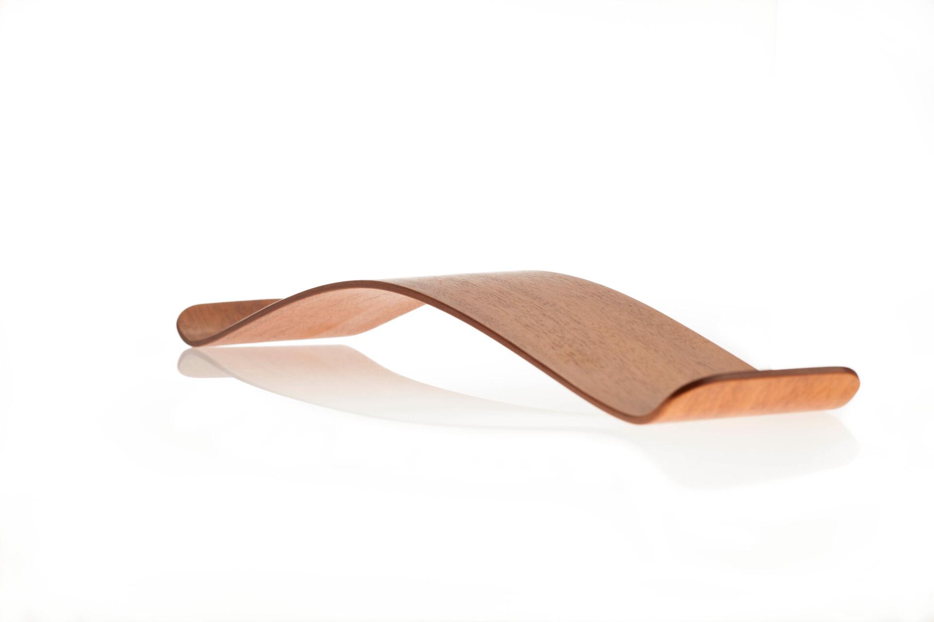 Curved wooden board with a smooth surface and light brown finish, resting on a reflective white background.