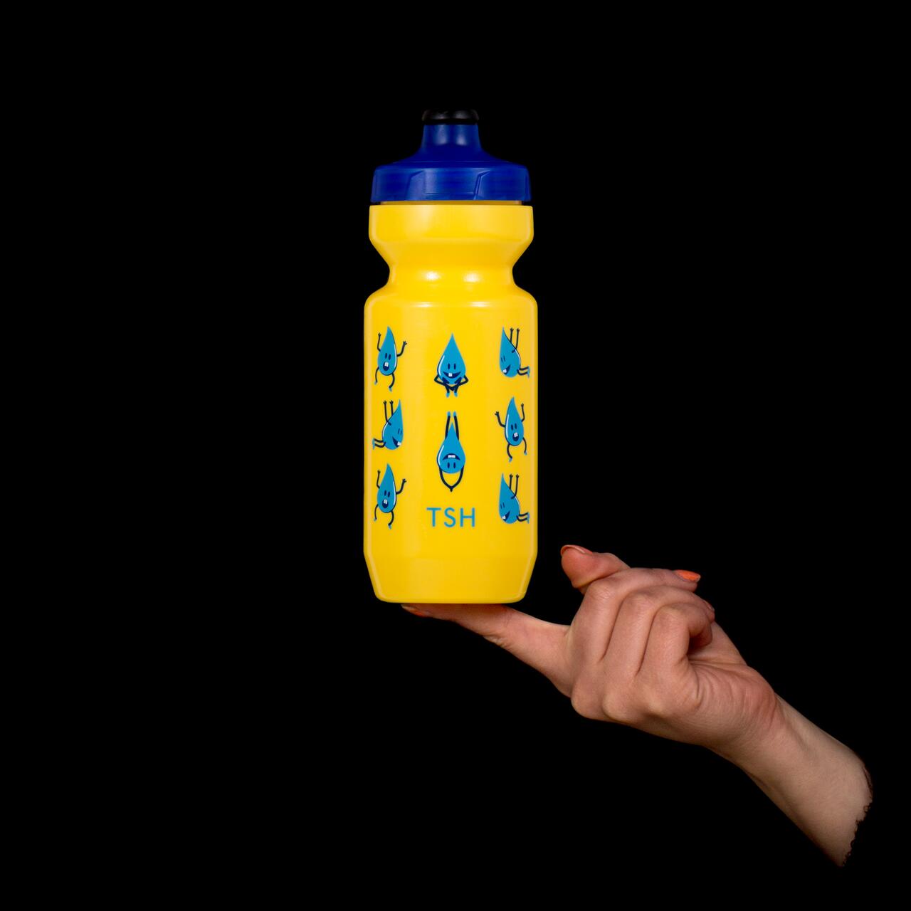 Yellow water bottle with blue cap and cartoon characters, balanced on a fingertip against a black background.