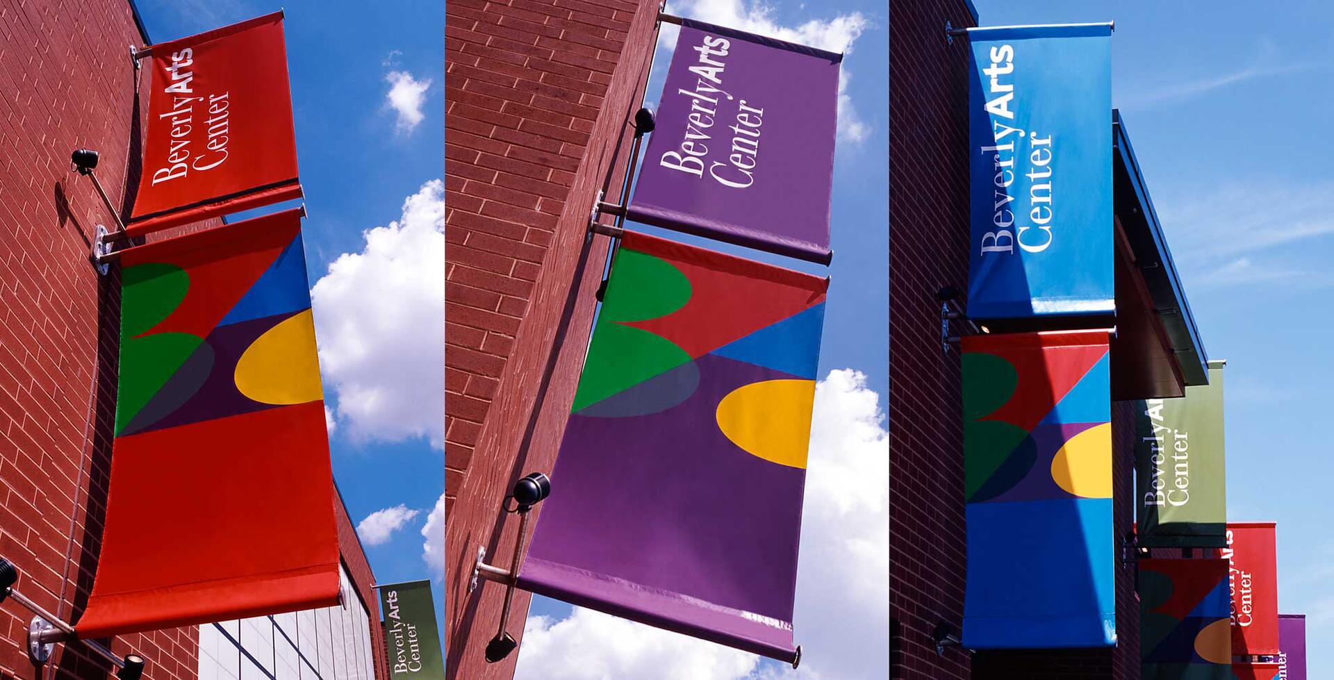 Colorful banners with abstract designs hang from brick walls under a blue sky, each labeled with "Beverly Arts Center" in white.