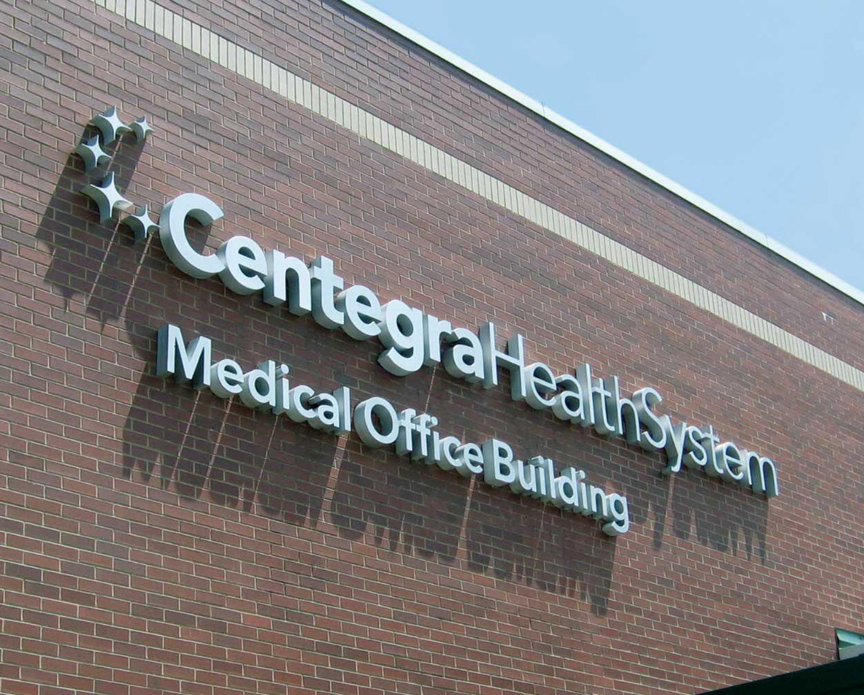 Centegra Health System Medical Office Building sign on a brick wall against a clear blue sky.