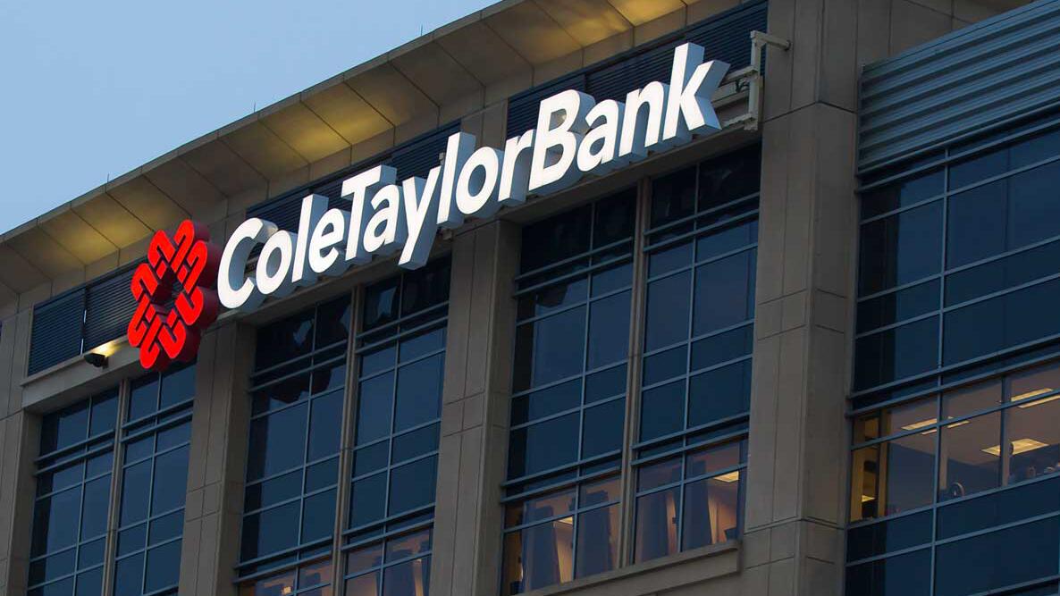 Building facade with large windows and the words "ColeTaylorBank" in illuminated white letters. A red logo appears beside the name against a darkening sky.