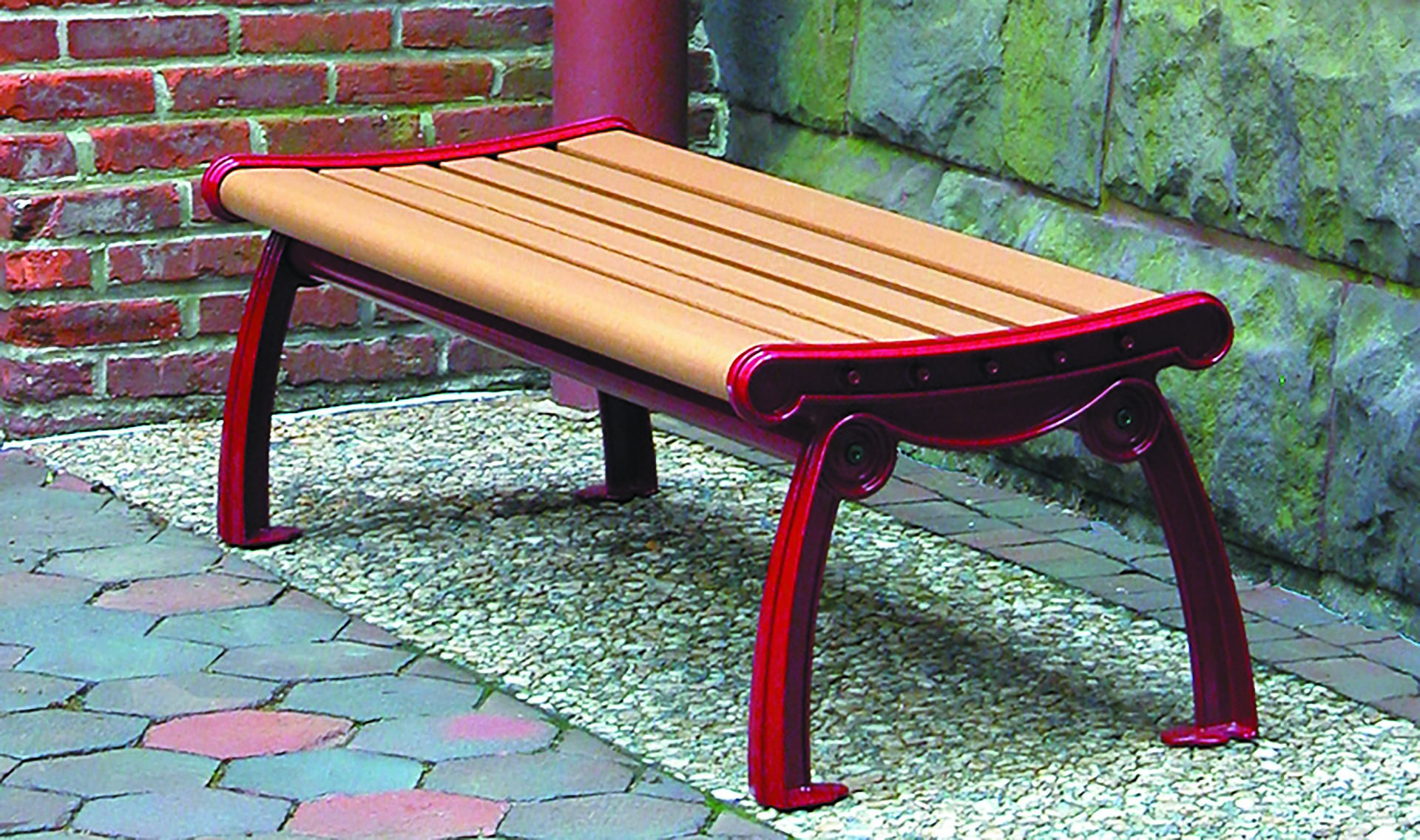 Wooden bench with red metal frame against a brick and stone wall on a mosaic-patterned sidewalk.
