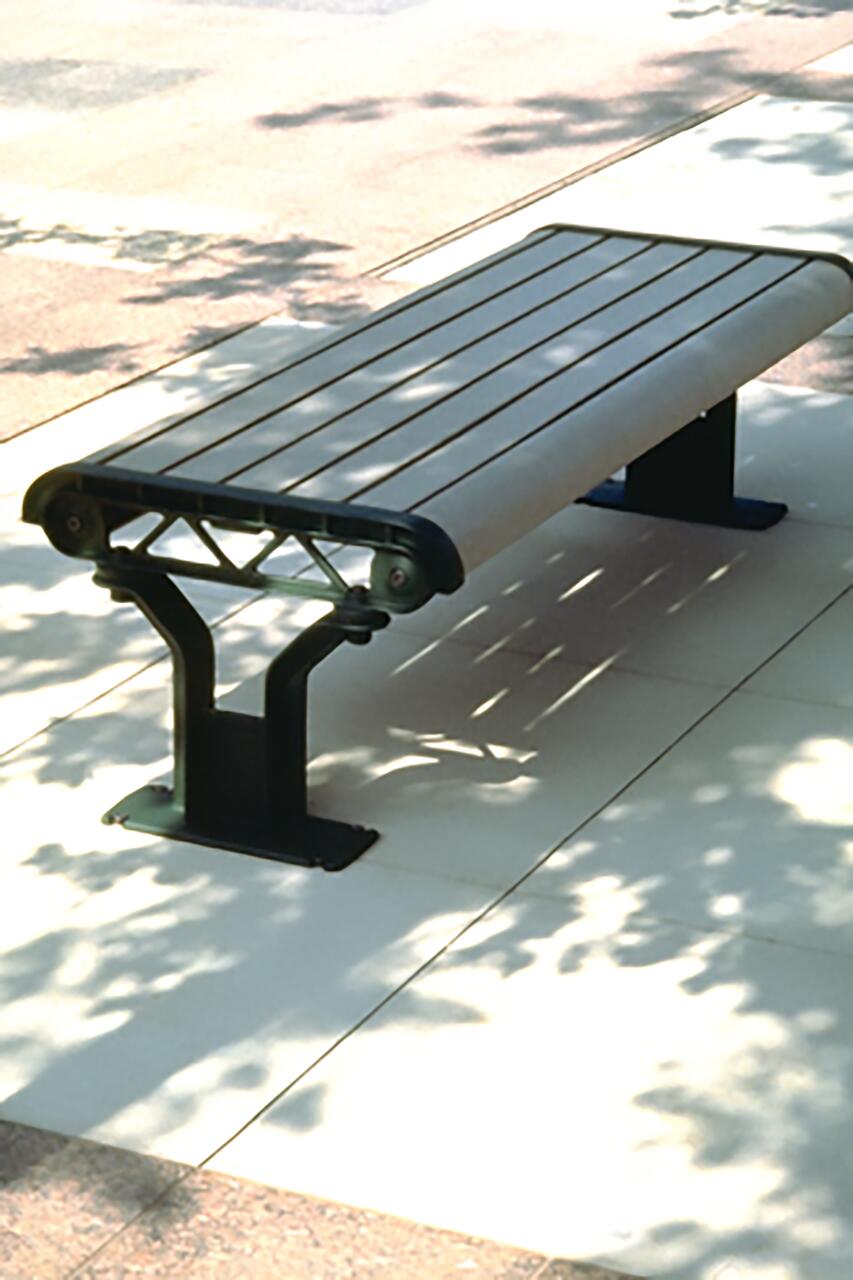 A metal and wood bench on a sunlit, shadow-dappled sidewalk.