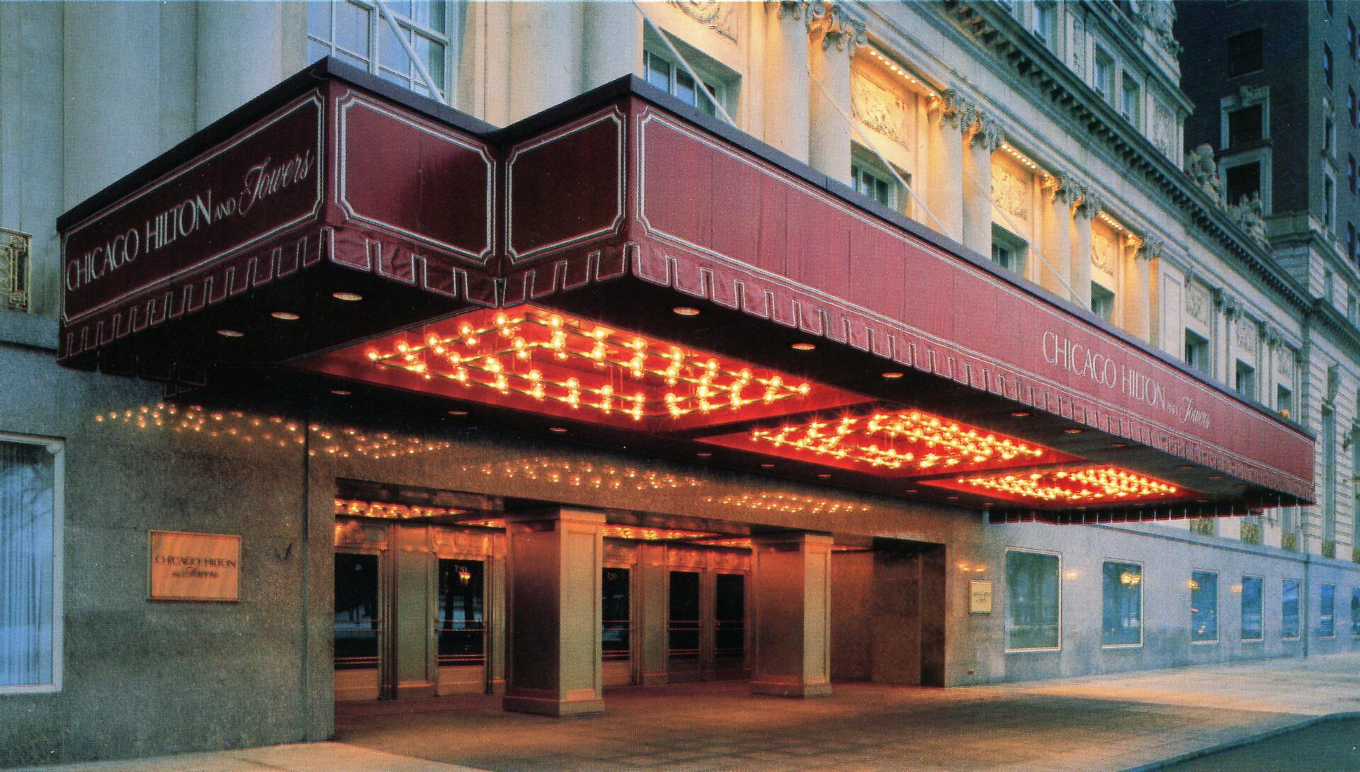 Elegant hotel entrance with a red awning and warm lights at dusk, featuring ornate architectural details above the doors.