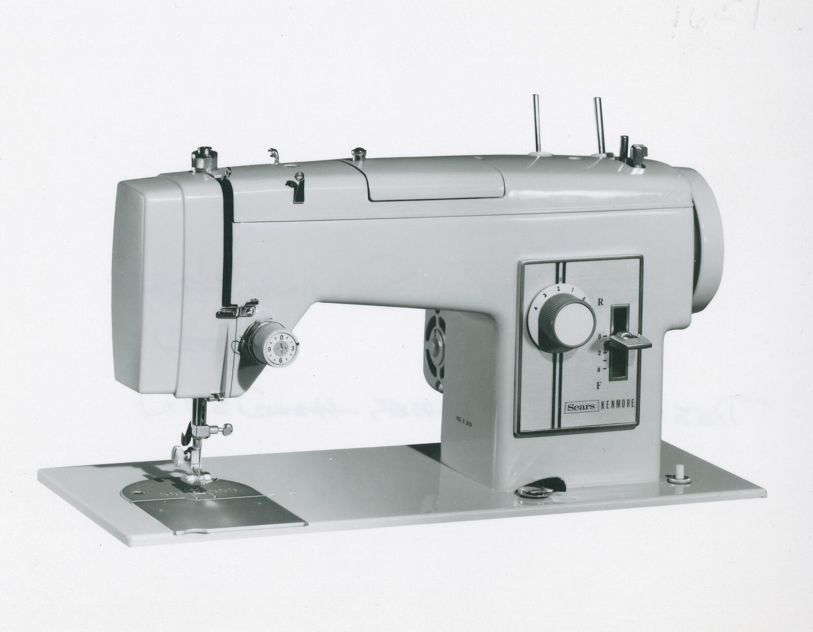 Vintage Sears Kenmore sewing machine with control knobs and levers on the front, set on a flat base.
