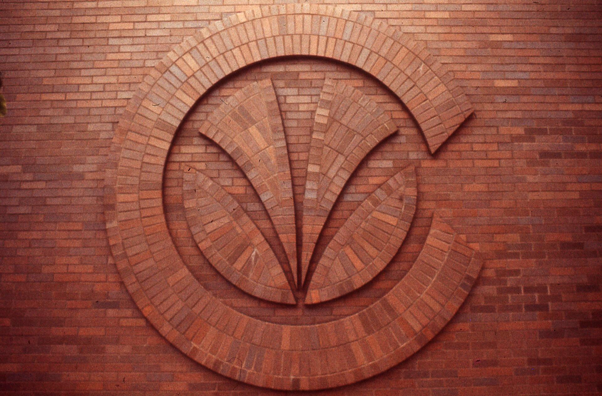 Brick wall with a large, circular, fan-like decorative pattern formed by overlapping bricks in varying shades of red.