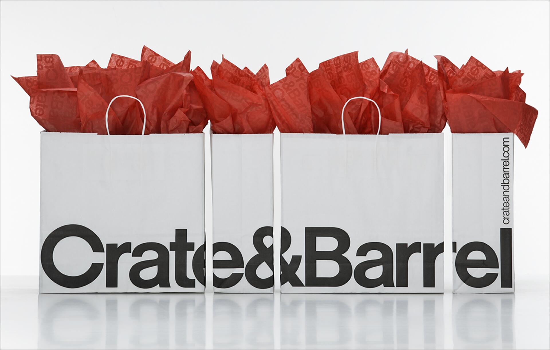 Three Crate & Barrel shopping bags filled with red tissue paper, arranged side by side.