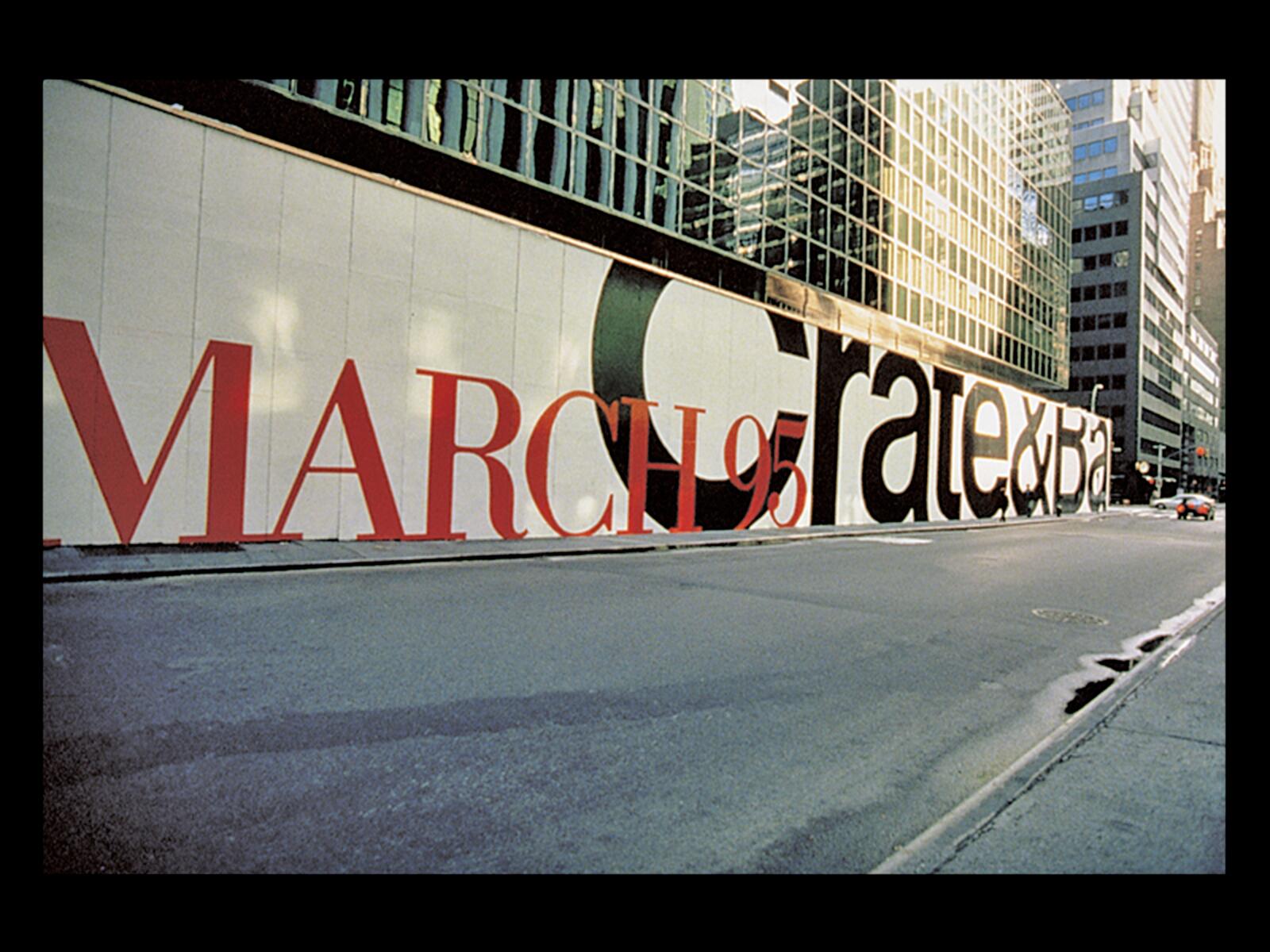 Large bold lettering on a city building facade reads "MARCH 95" in red and "Crate" in black. The street view includes tall reflective glass buildings under a clear sky.