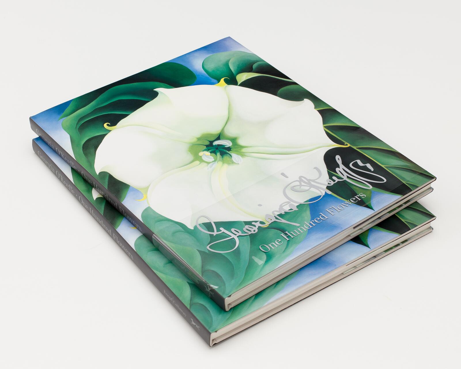 Two stacked hardcover books featuring a large white flower with green leaves and a blue background on the cover.