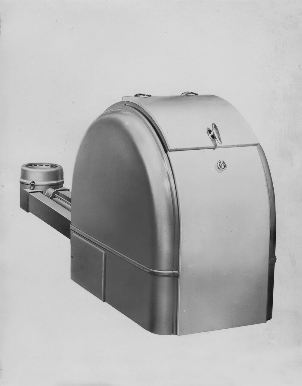 Black and white photograph of a vintage, metallic, dome-shaped machine with a lever on one side and a round attachment.