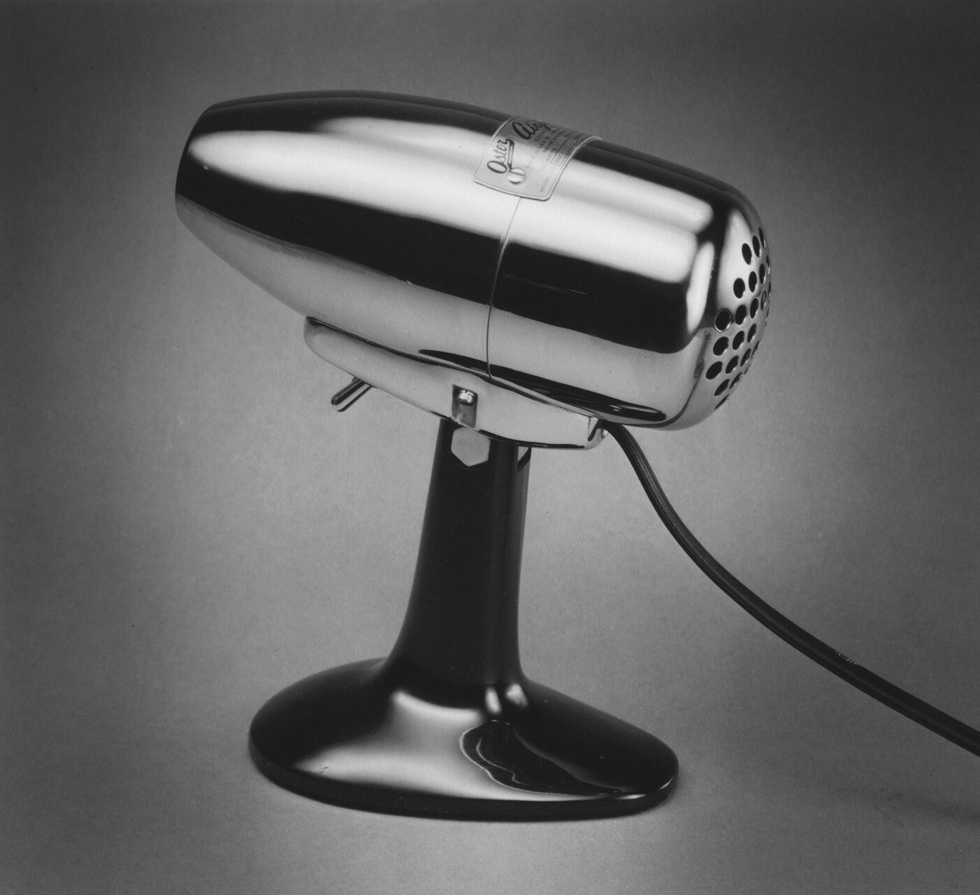 Vintage chrome tabletop microphone with a sleek, shiny finish, resting on a black stand, captured against a plain gray background.