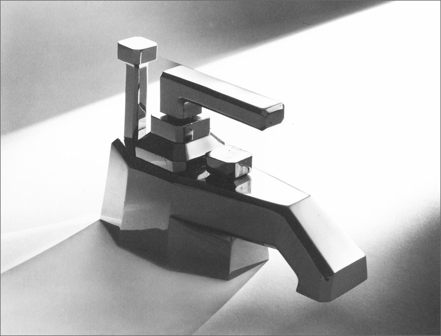 Black and white photograph of a modern, geometric chrome faucet with angular design, casting a sharp shadow on a smooth surface.