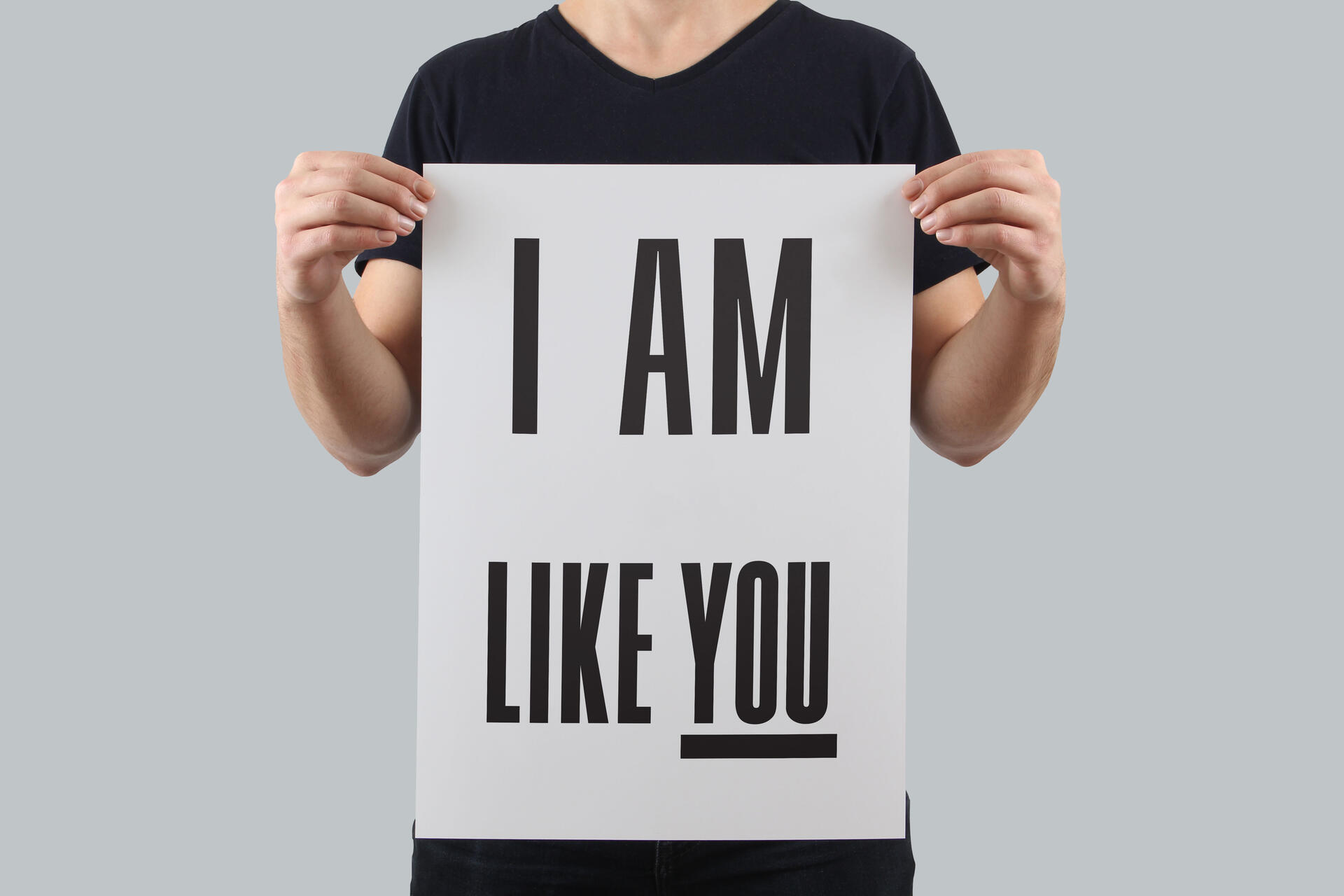 Person in a black shirt holding a white sign with bold text saying "I AM LIKE YOU."
