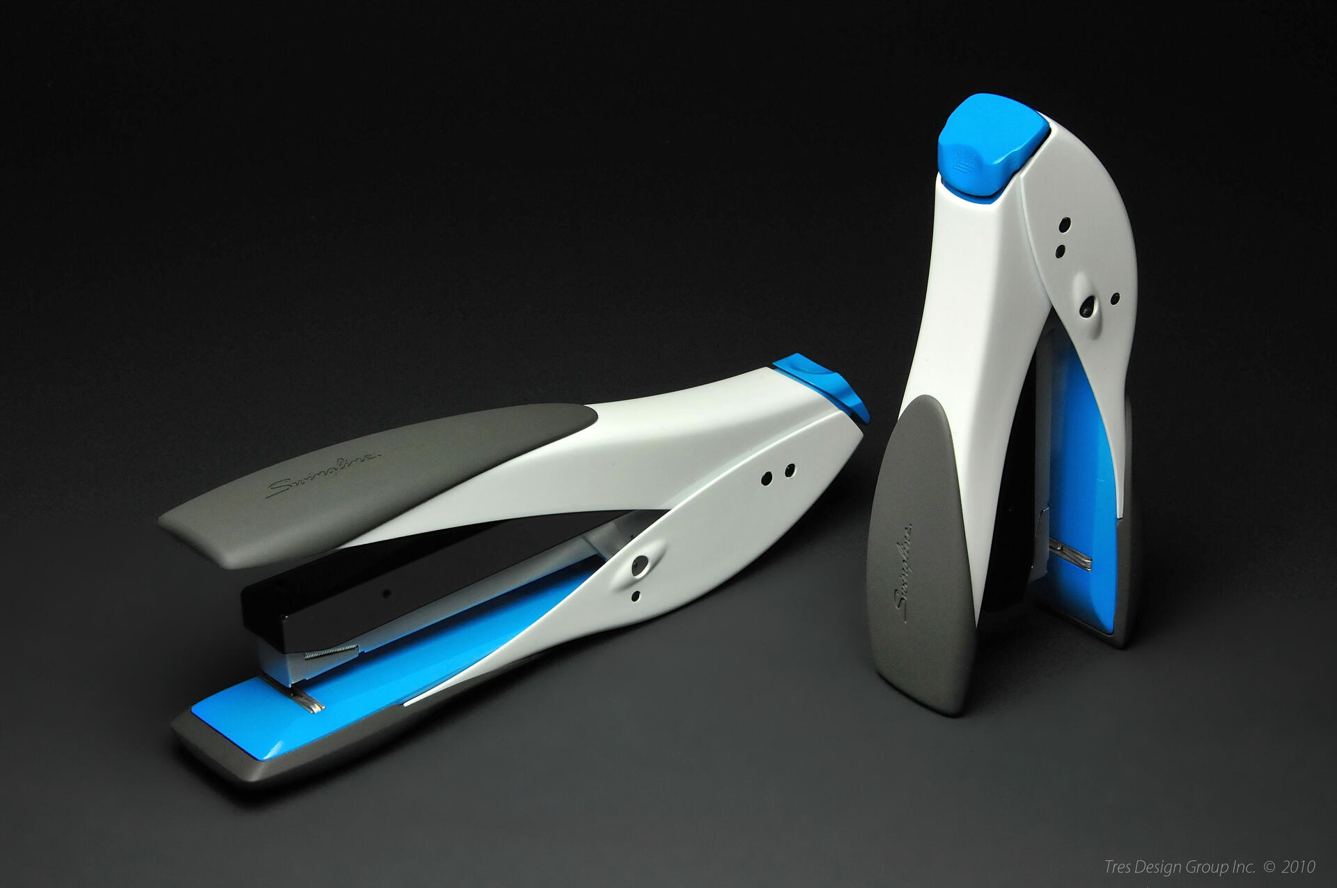 Two modern staplers in white, gray, and blue on a black background, one lying down and one standing.