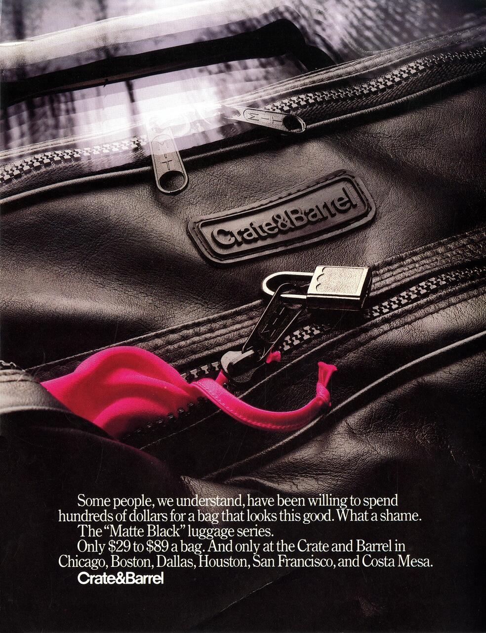 Black leather luggage bag with Crate & Barrel logo and silver zippers, partially open to reveal a bright pink interior.
