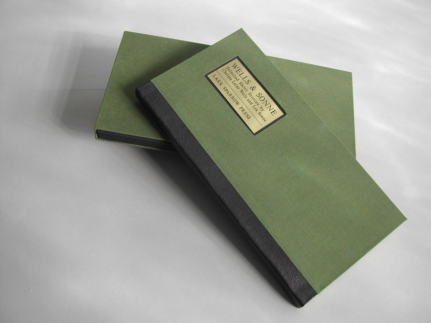 Two green hardcover books with black spines, one partially over the other, on a light gray surface. A gold label is affixed to the top book's cover, displaying text.