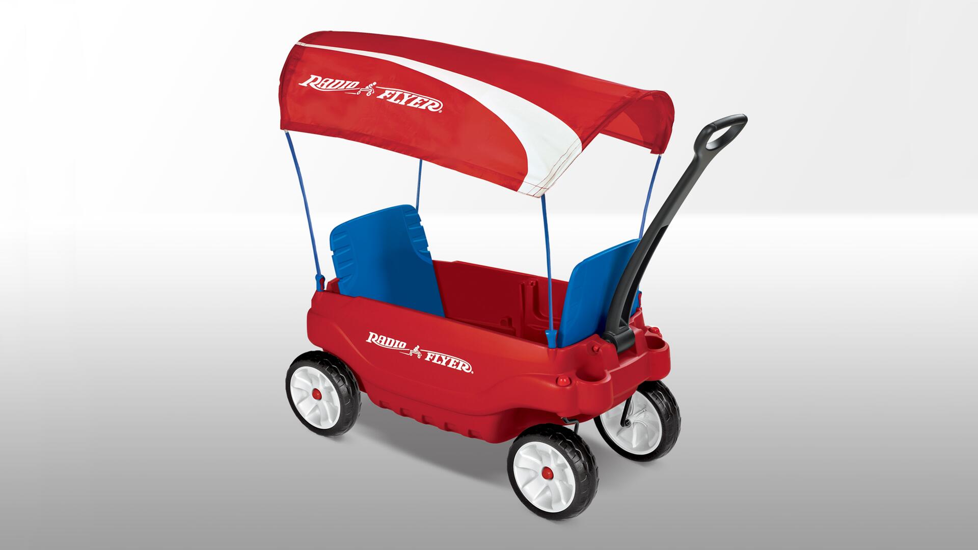 Red plastic children's wagon with canopy, two blue seats, and black handle. The wagon has four white wheels and "Radio Flyer" branding on the side.