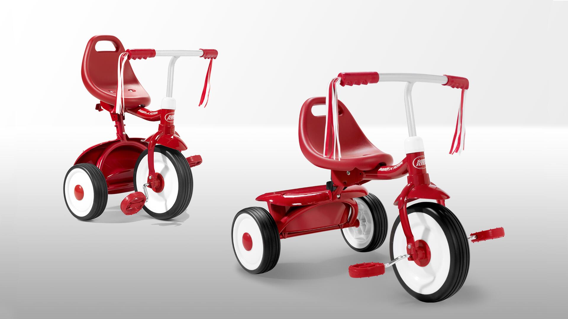 Red and white children's tricycle with streamers on the handlebars, red seat, and large white wheels on a light gray background.