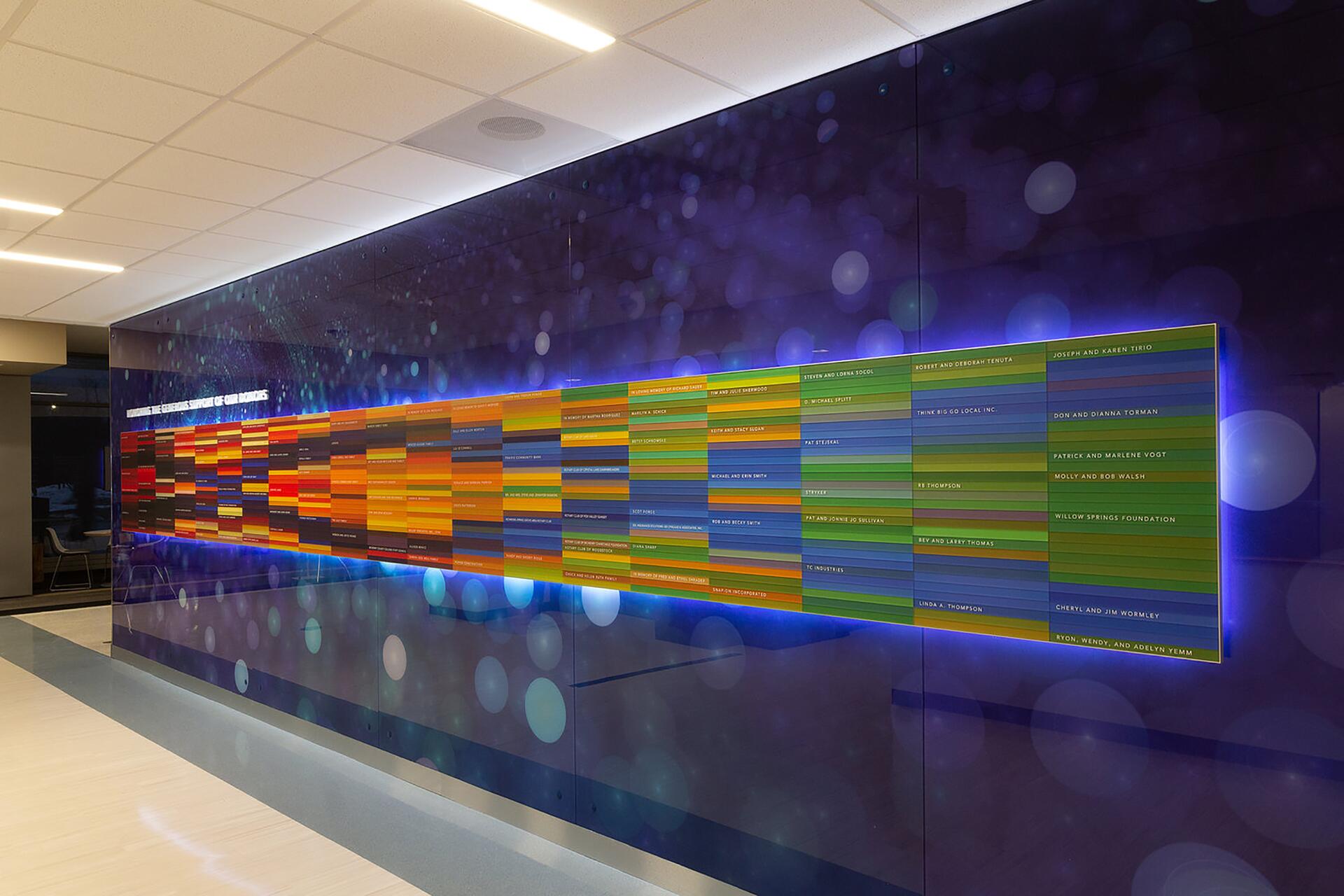 Colorful wall display with rows of names in a modern hallway, set against a purple background with floating light circles, creating a vibrant and futuristic atmosphere.