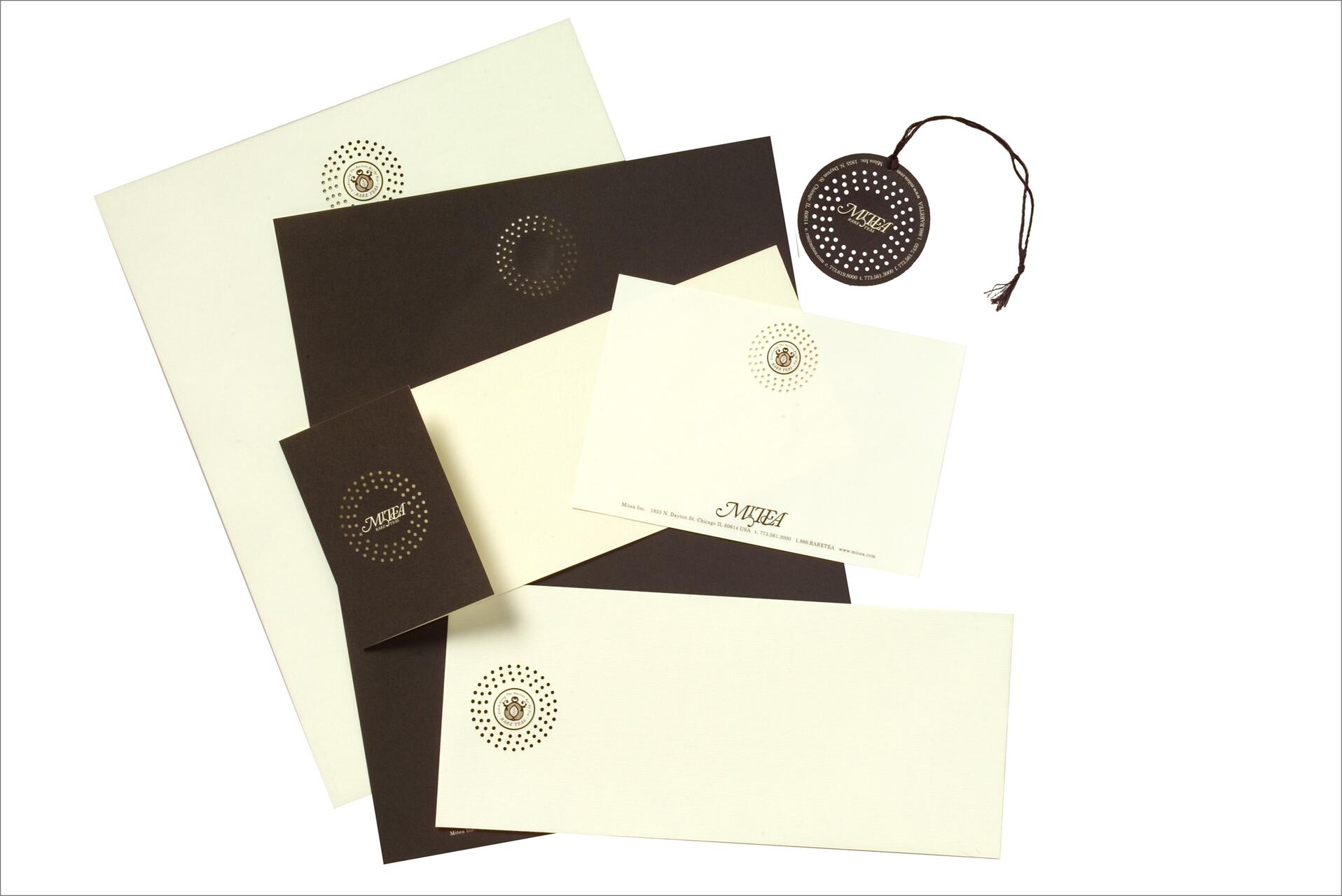 Stationery set with brown and cream-colored papers, envelopes, a small card, and a tag, featuring a dotted circular logo.