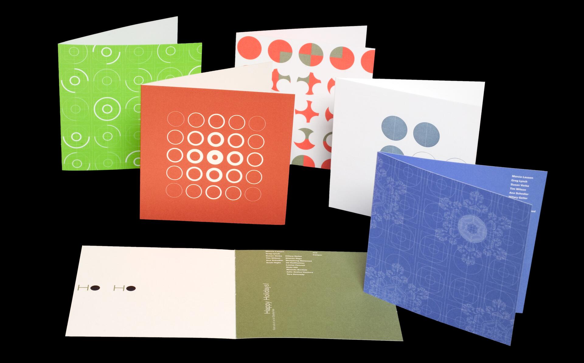 Colorful greeting cards featuring geometric patterns in green, red, blue, and white, arranged in a semi-circle against a black background.