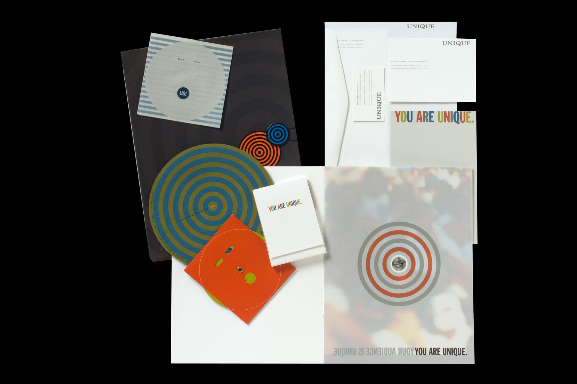 Stationery set with colorful circular patterns, envelopes, and cards featuring a message in multicolored text. The design has a modern, playful aesthetic with emphasis on uniqueness.