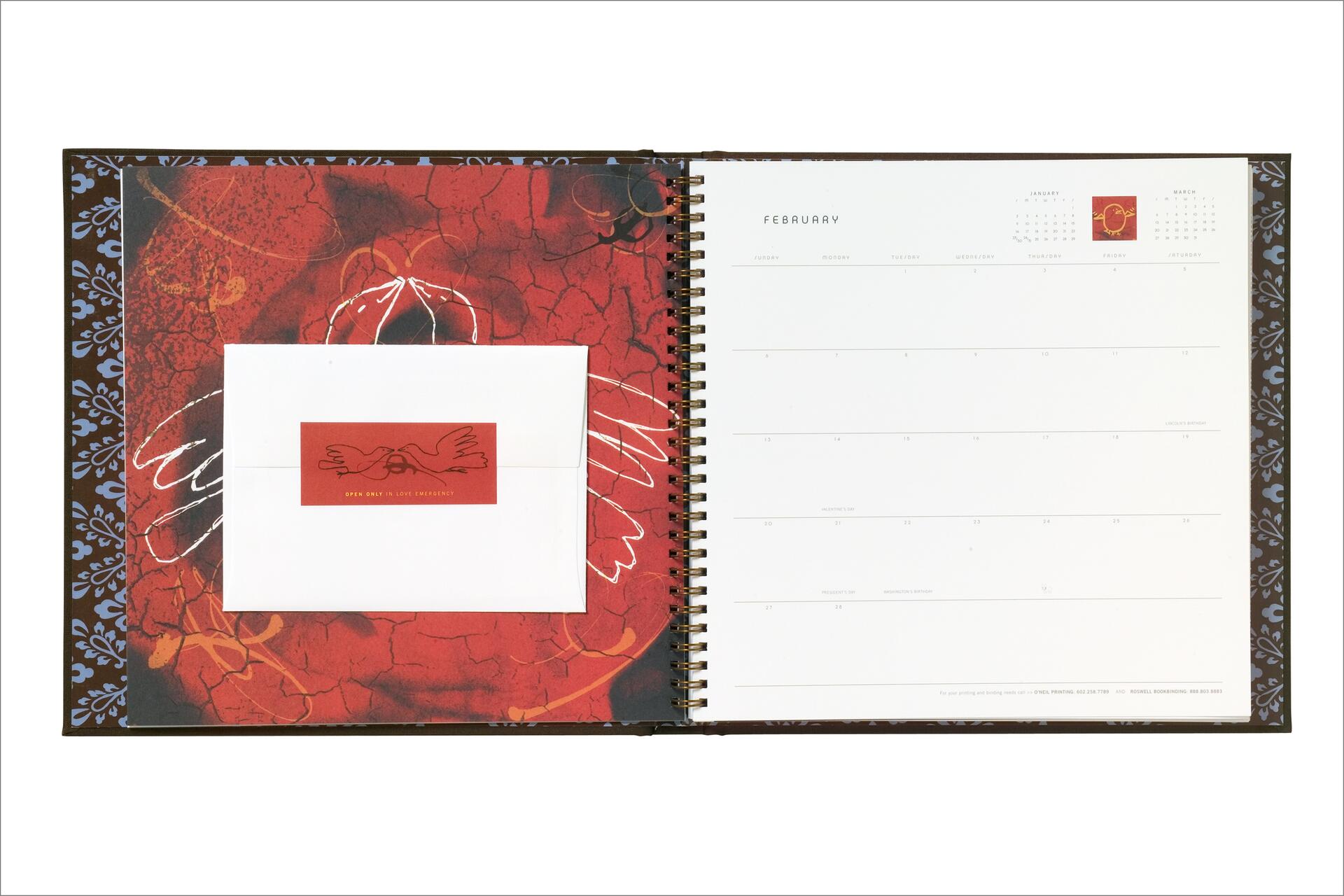 Open spiral-bound calendar showing February with an envelope on the left page, set against a red and black cracked pattern with white abstract lines. The right page is a blank calendar layout.
