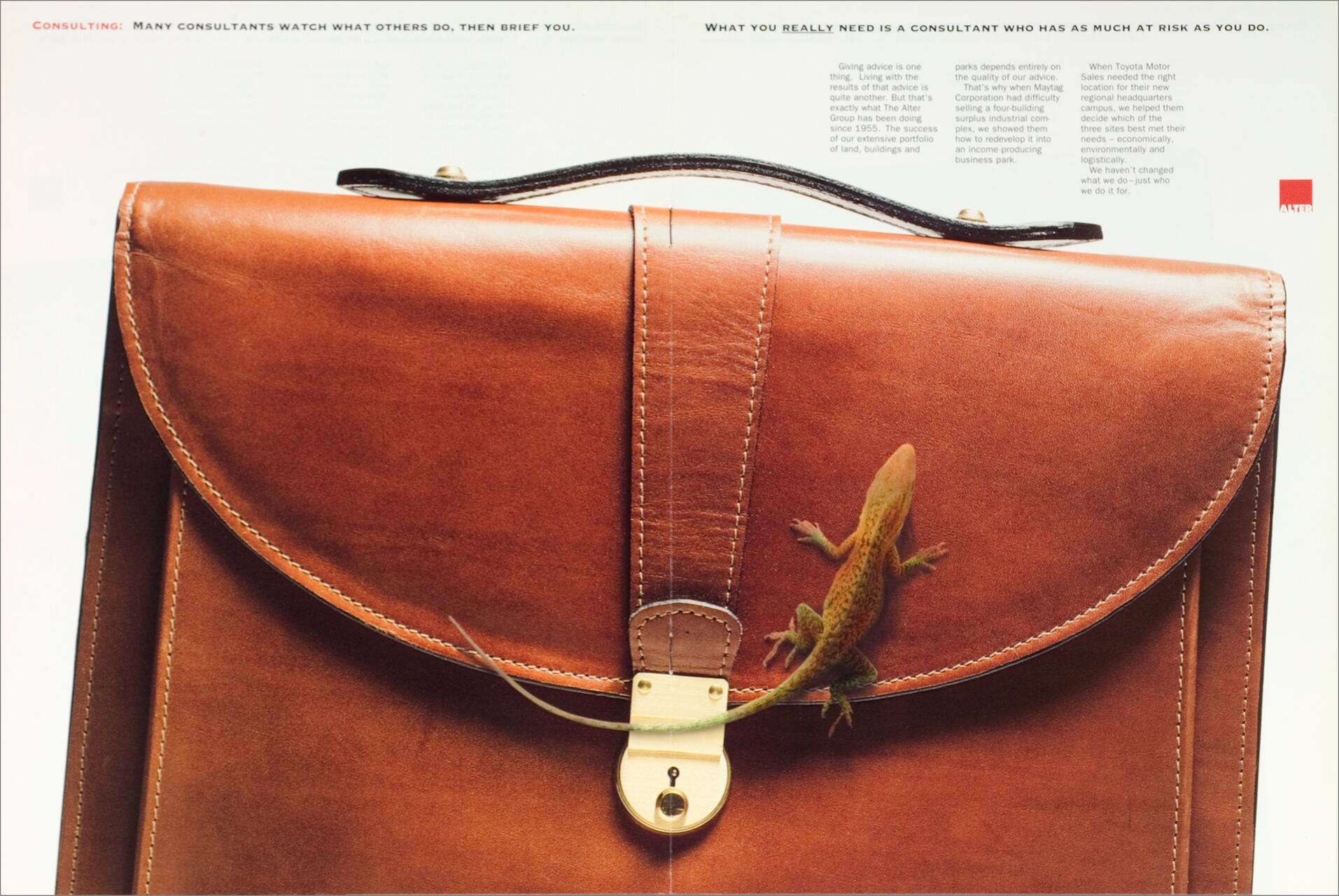 Brown leather briefcase with a small lizard climbing on the front flap. The lizard is near the gold lock. Text elements are present in the background.