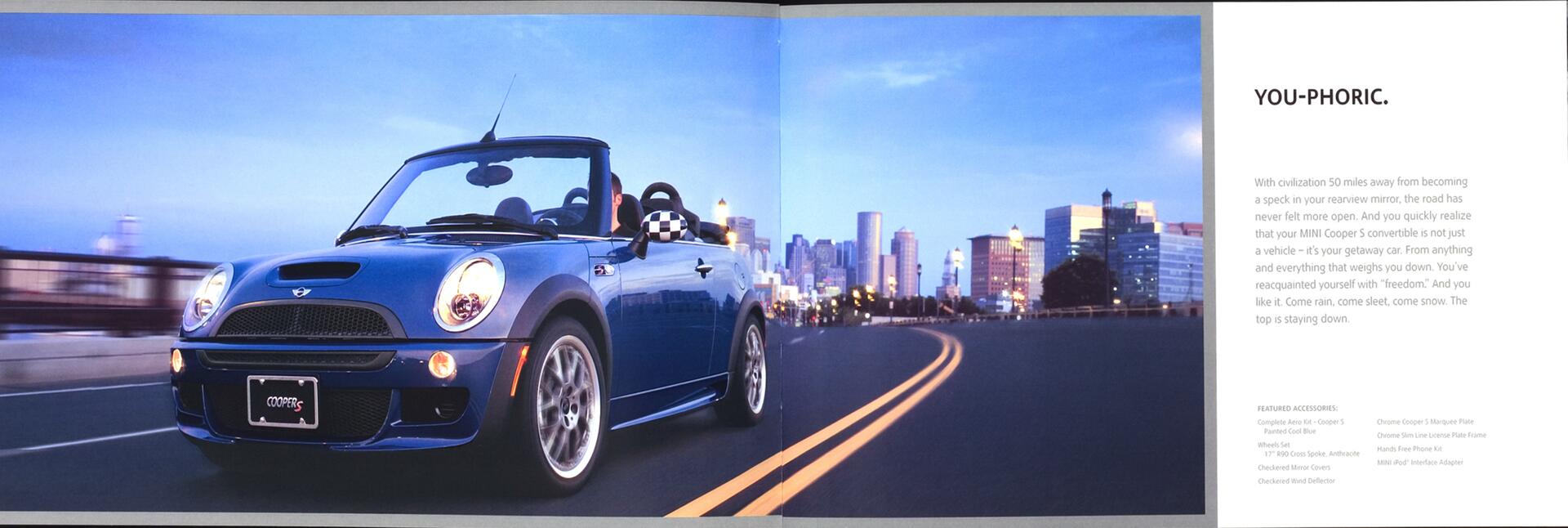 A blue convertible car drives on an empty highway at dusk, with a city skyline in the background. The sky is a gradient of blue, and the road curves slightly to the right.