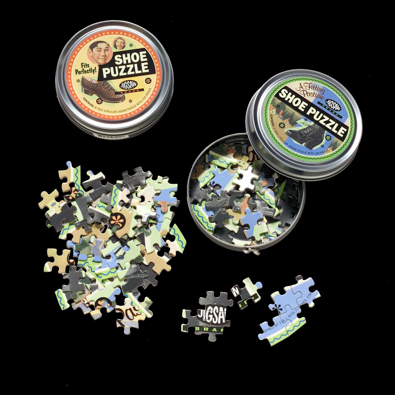 Jigsaw puzzle pieces scattered around two metal tins labeled "Shoe Puzzle" on a black background.