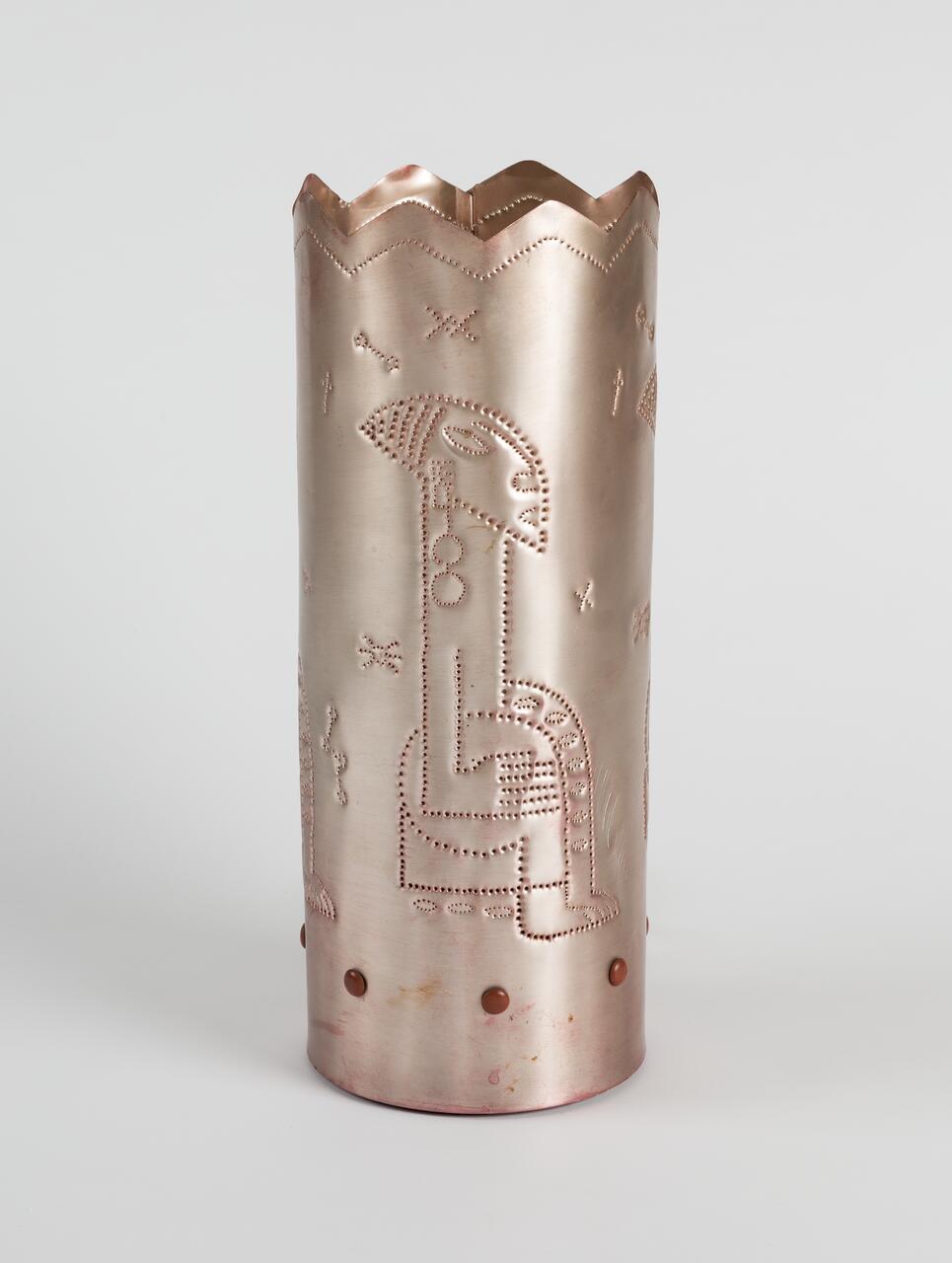 Copper cylindrical sculpture with perforated geometric designs and a scalloped top edge, featuring abstract patterns and figures etched across the surface.