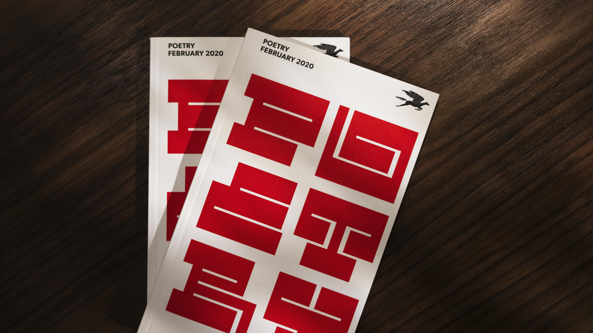 Two poetry magazine covers with bold red geometric patterns, dated February 2020, placed on a dark wooden surface with a flying bird silhouette at the top right corner.