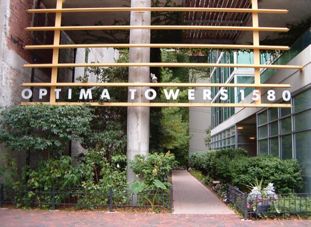 Entrance to Optima Towers, featuring a modern architectural design with horizontal beams and lush green landscaping.