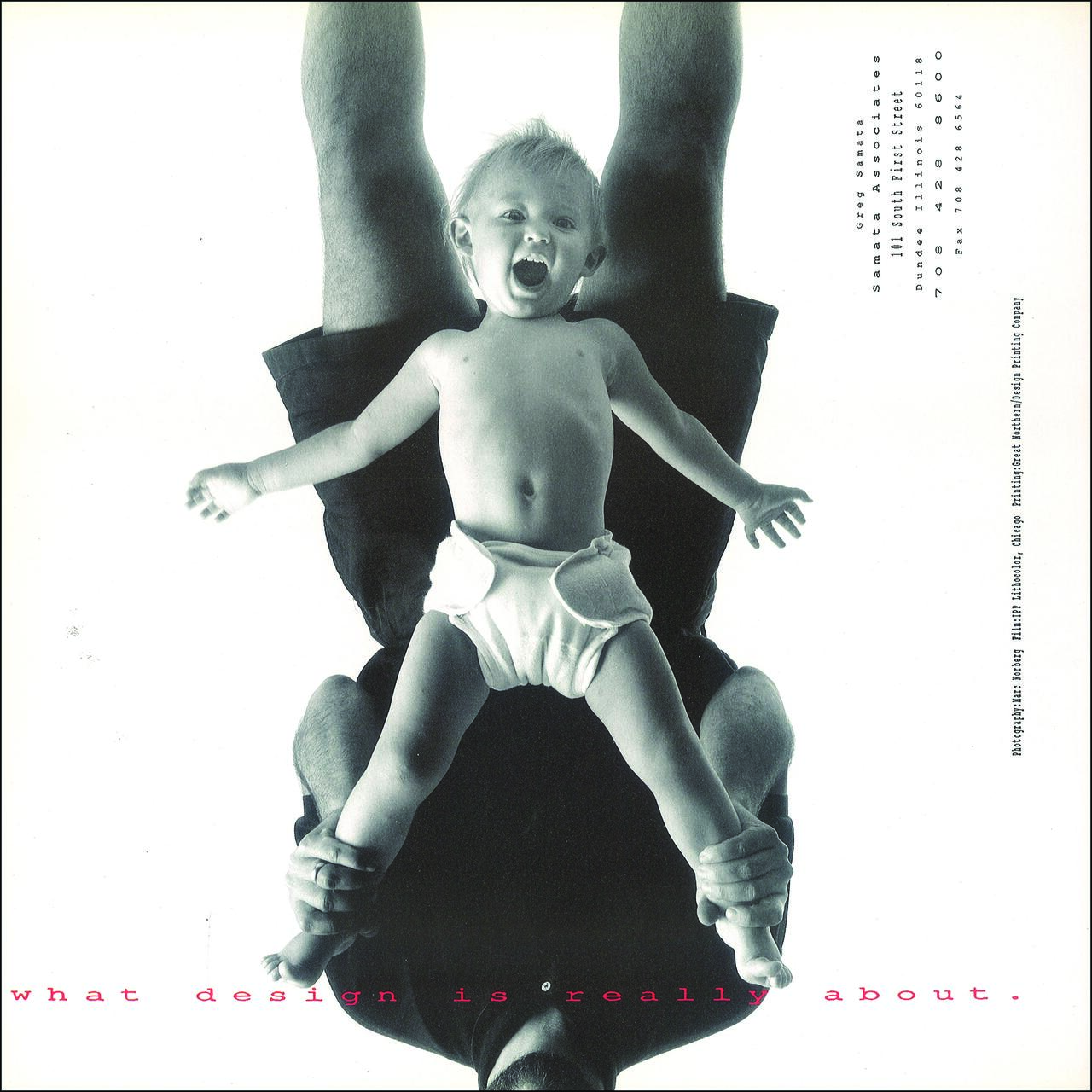 A black and white photo of a person lying on their back, holding a smiling baby above them. The baby, wearing a diaper, spreads its arms joyfully. The photo is viewed upside down, with pink text at the bottom.