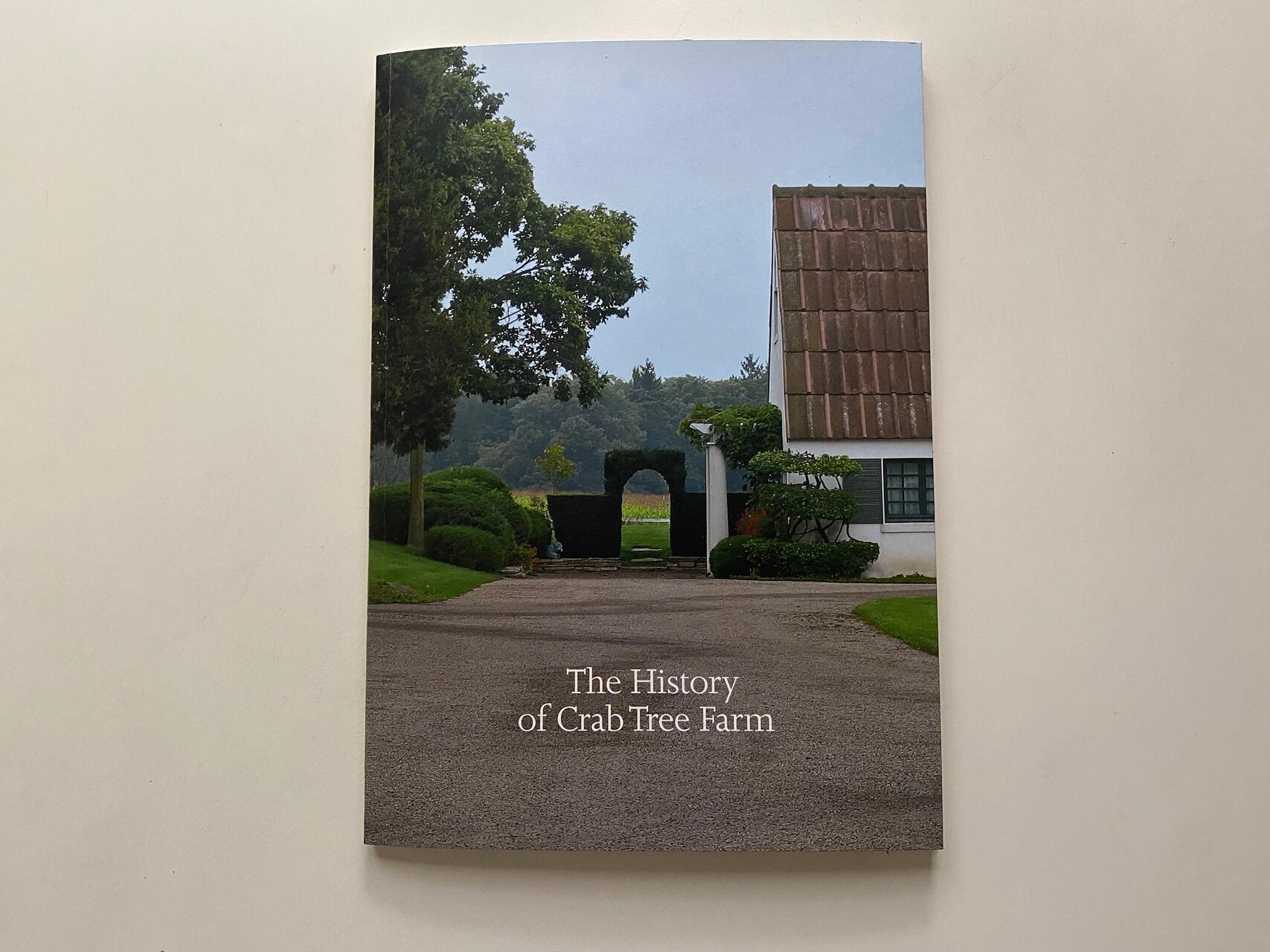 Book cover featuring a rural scene with a white building, greenery, and a pathway. Text reads "The History of Crab Tree Farm."