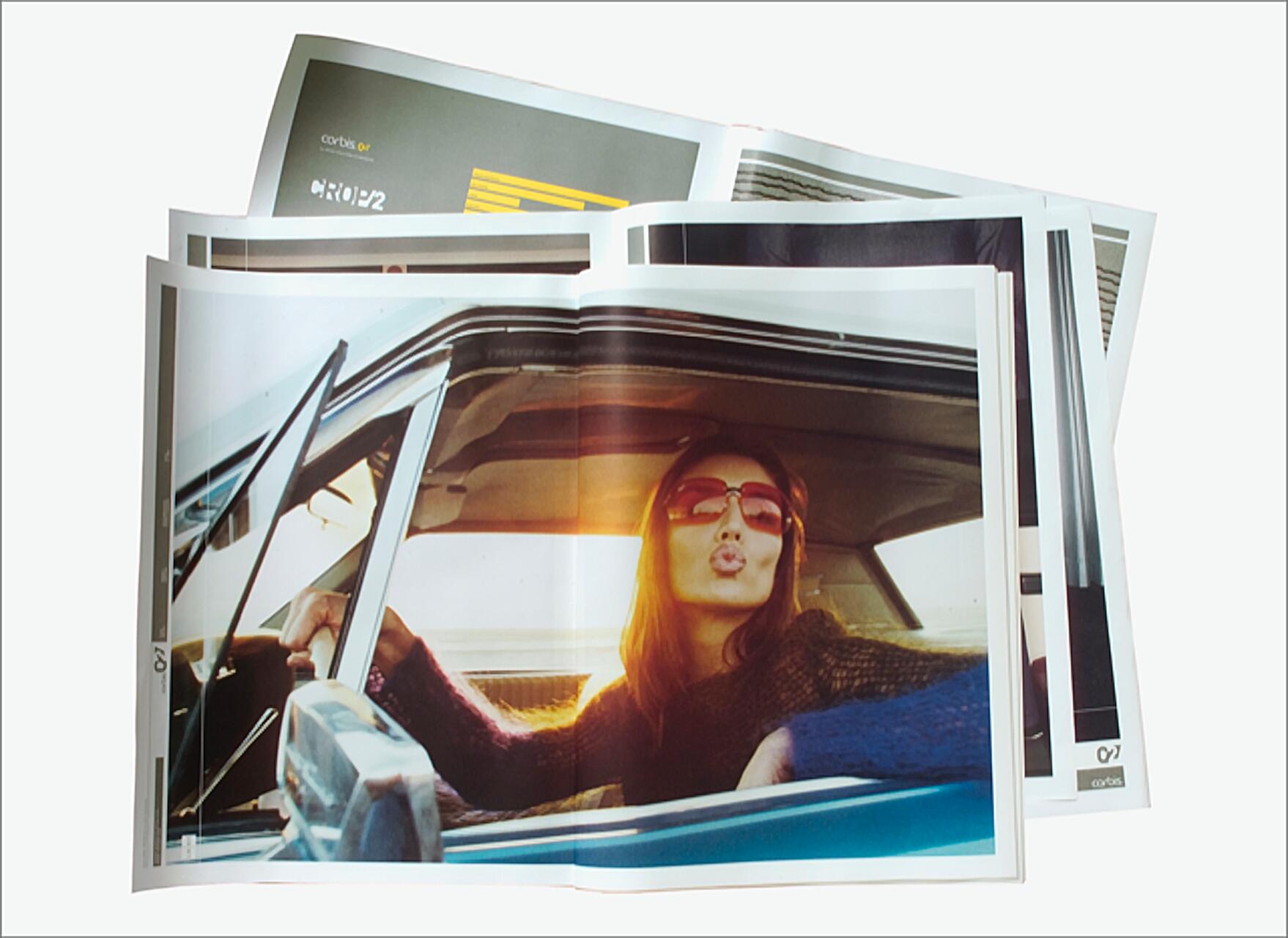 Magazine pages showing a photograph of a person in sunglasses, seated in a car, blowing a kiss towards the camera. The sun sets in the background, creating a warm glow inside the vehicle.